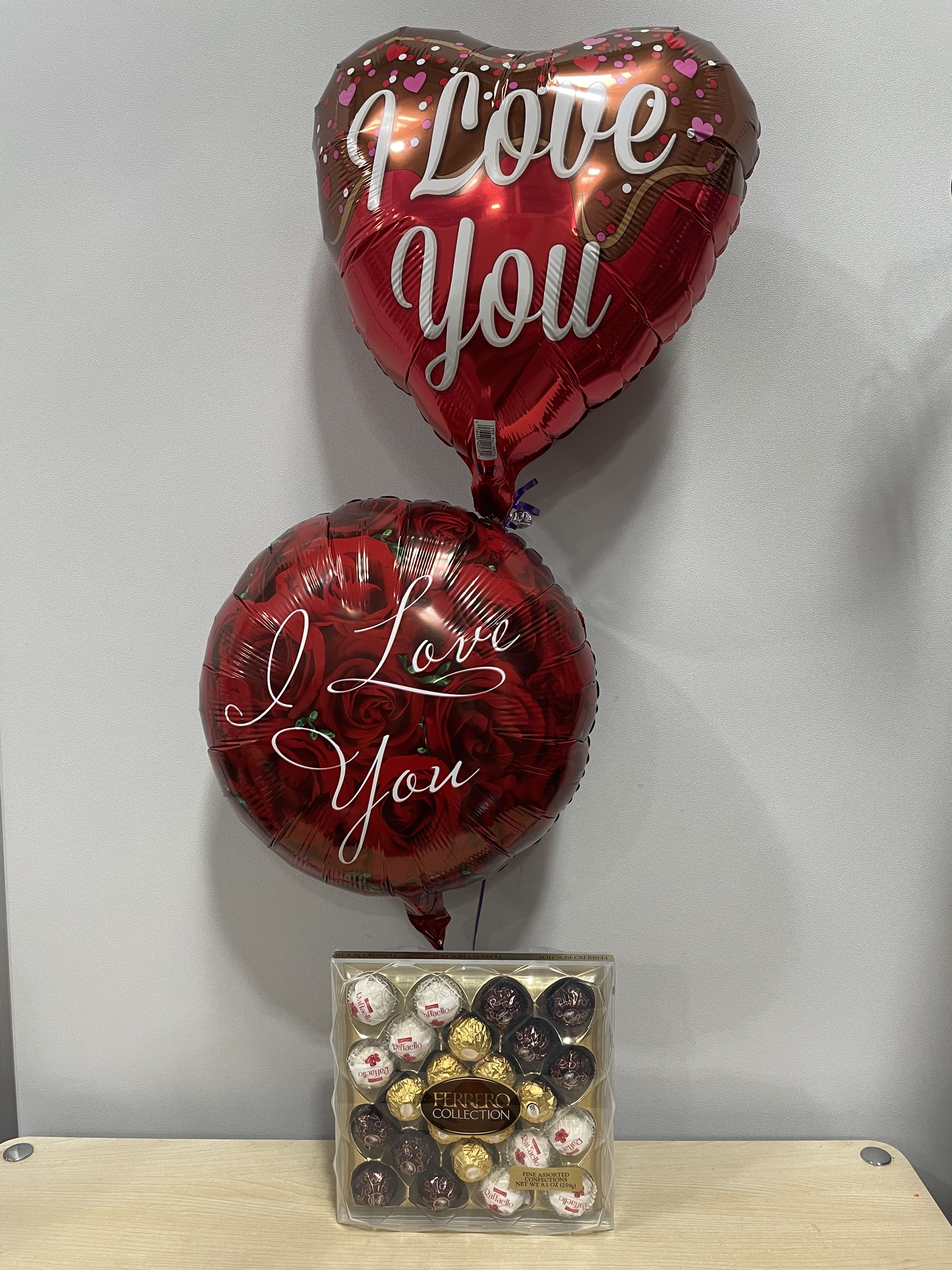 Two heart-shaped balloons with love messages above a box of Ferrero chocolates