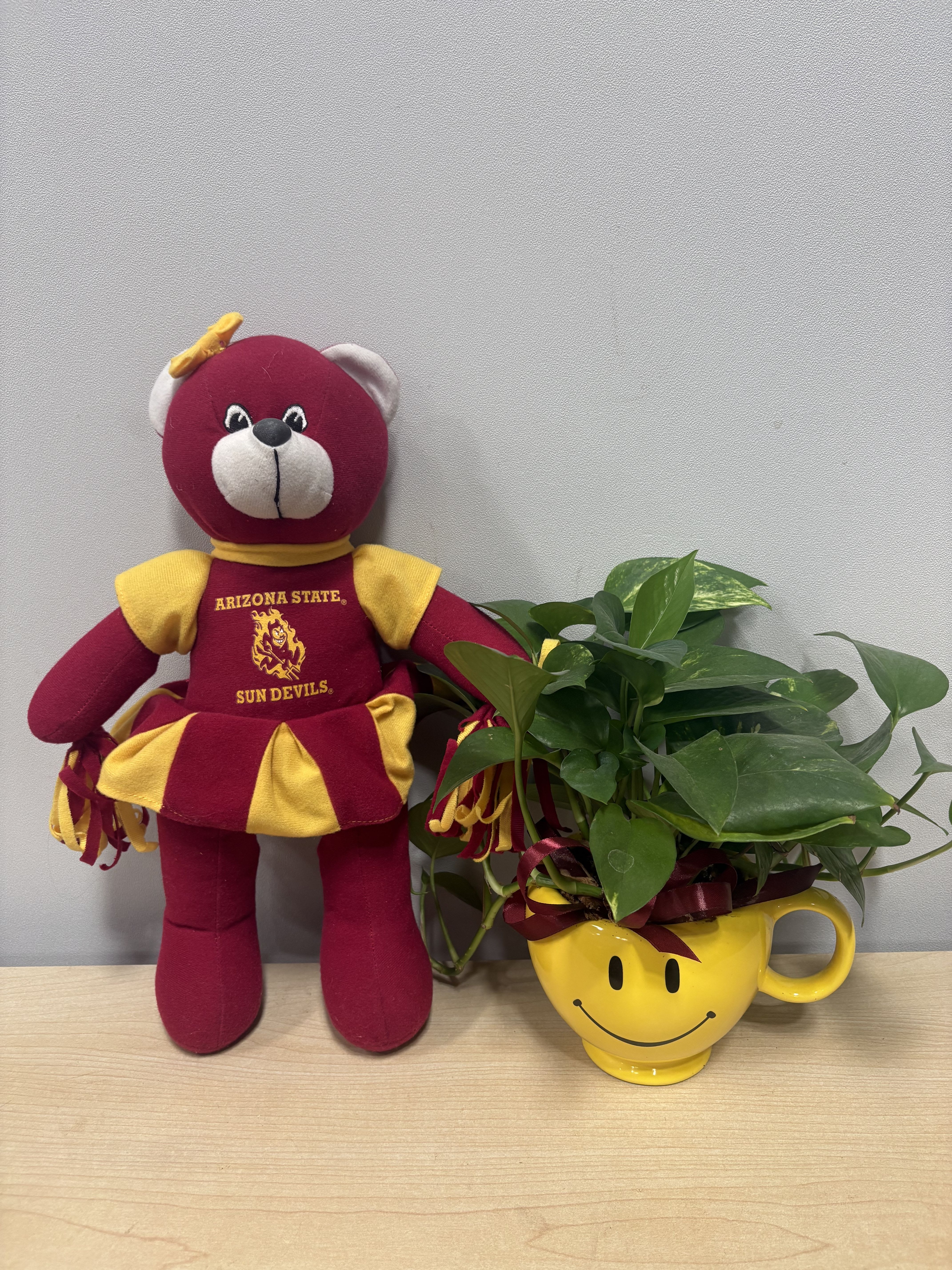 Plush bear beside a leafy plant in a yellow smiley-face mug