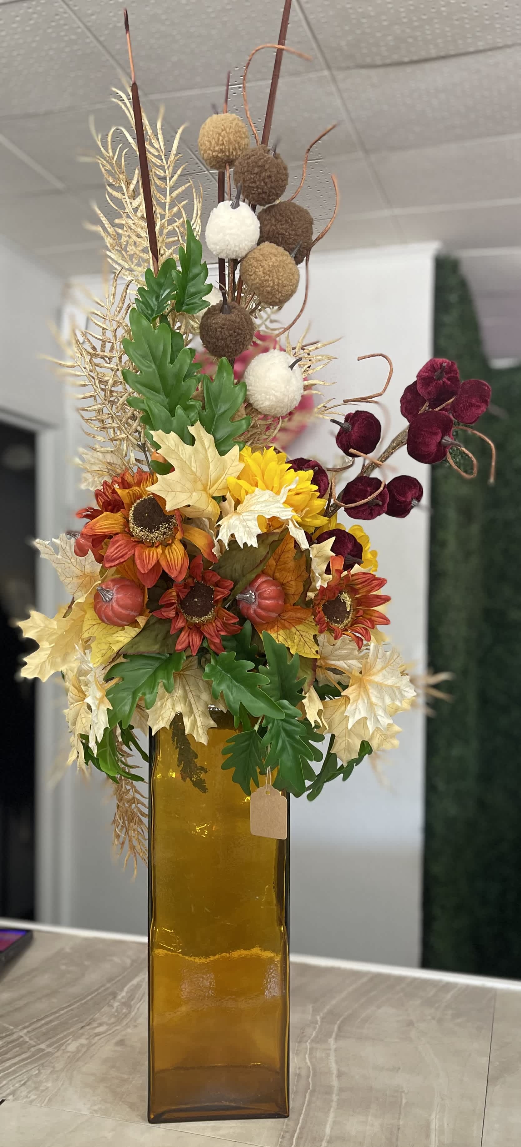 Tall autumn floral arrangement in an amber glass vase