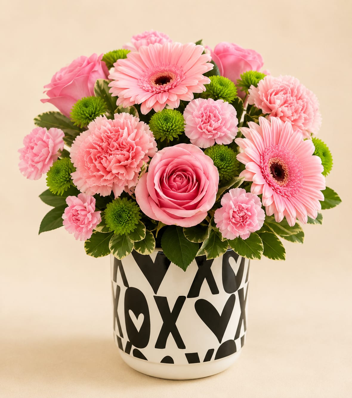 XoXo Floral - Soft pink roses and gerbera daisies mingle with ruffled carnations in a compact, rounded bouquet that reads cheerful and romantic - the perfect anniversary arrangement or birthday surprise. Designed for "just because" , XoXo Floral sends a playful, affectionate message that will make the person you're thinking of feel seen and adored.  Bright green button mums add lively contrast and texture against the soft pinks and whites, while the bold black-and-white ceramic vase - decorated with heart and X motifs - gives the design a modern, giftable edge. Arranged tightly for a full look, this piece presents a pleasing mix of soft petals and crisp color pops in a durable keepsake vase that fits tabletops and desks.  Choose this arrangement when you want someone to smile on their birthday, mark an anniversary, or receive a sweet "thinking of you" moment; it's the kind of bouquet that brightens a room and lingers in memory. The ceramic vase is reusable and the flowers benefit from fresh water and daily trimming of stems for longest enjoyment.