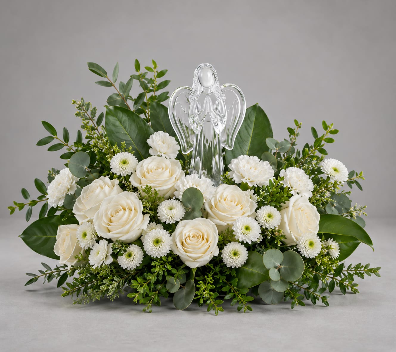 Light of Love Angel - Light of Love Bouquet offers a serene expression of the season. Elegant white roses and winter greens surround with this keepsake Crystal Angel-perfect for any sympathy, or spiritual décor. Light of Love Bouquet includes white roses, white carnations, white miniature carnations, and white button spray chrysanthemums. Accented with dusty miller, spiral eucalyptus, magnolia leaves, cedar, and Douglas fir and a Crystal Angel for non winter months cedar, and Douglas fir will be replaced with regular greenery. 
