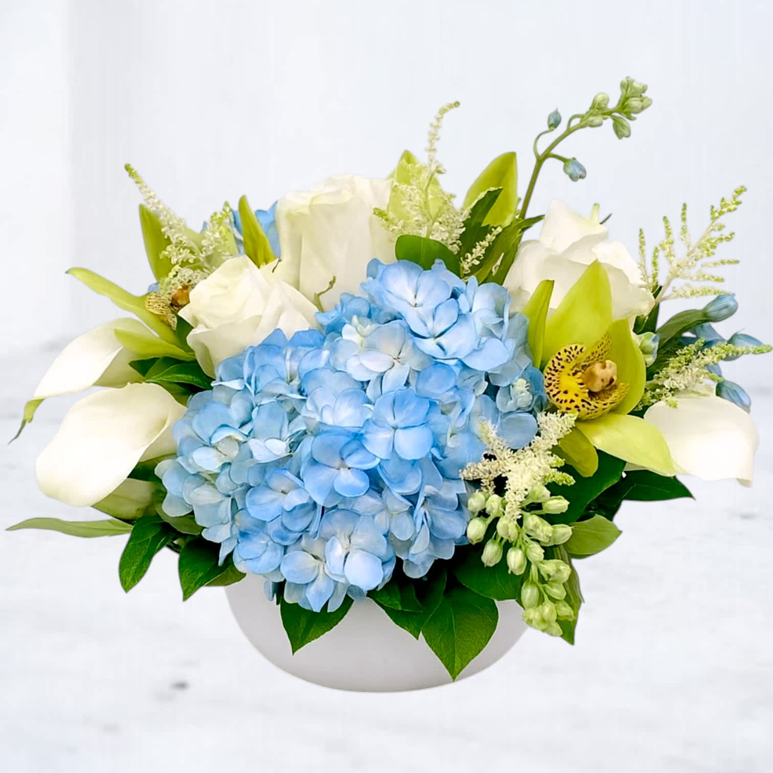Blue hydrangea and white orchids in a white bowl vase