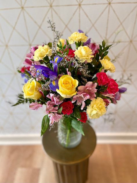 Mixed bouquet of roses, carnations, and purple flowers in a glass vase