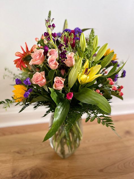 Mixed bouquet of pink roses, yellow lilies, and purple flowers in a glass vase