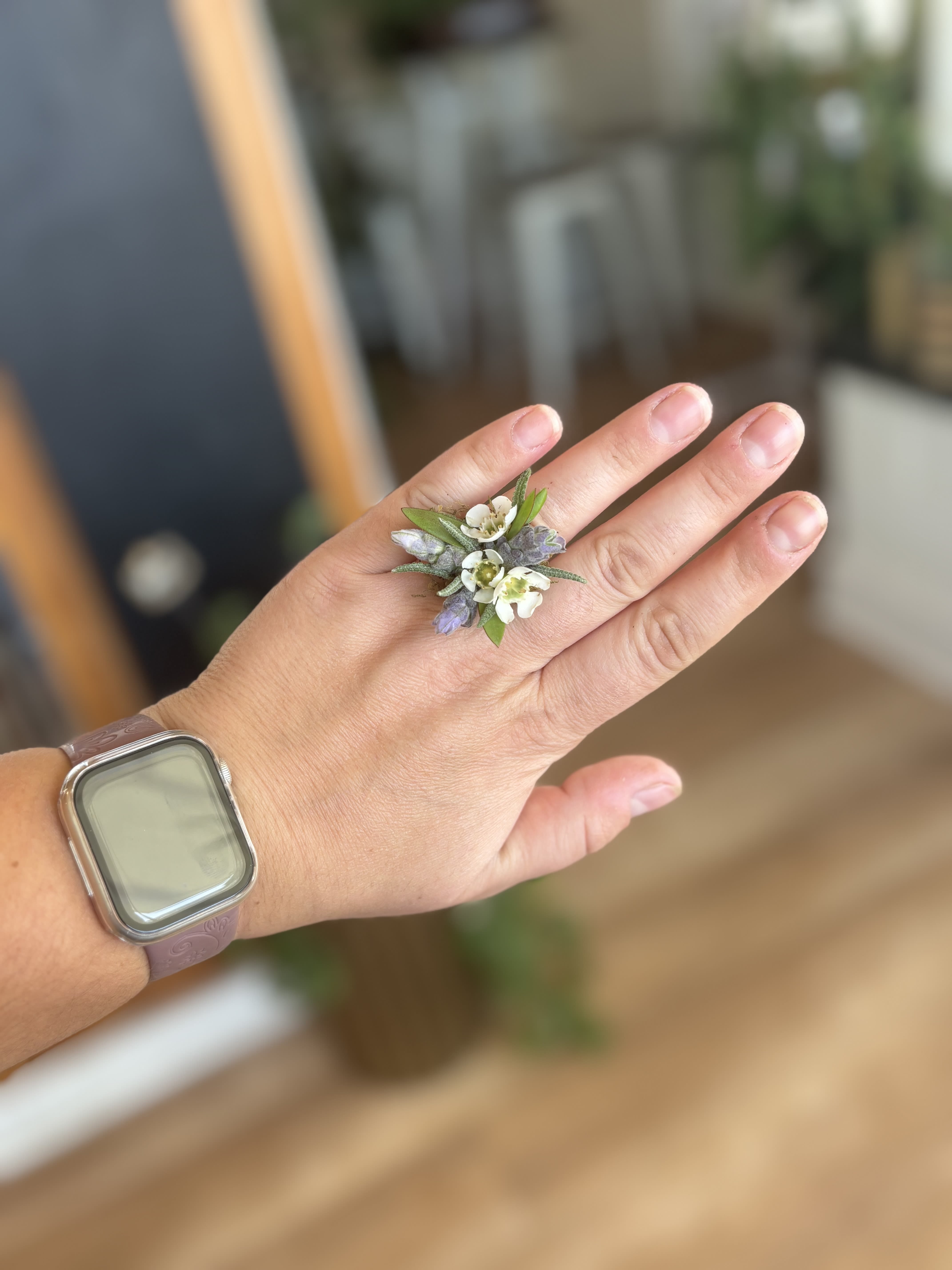 Hand wearing a small floral ring with white and lavender blossoms
