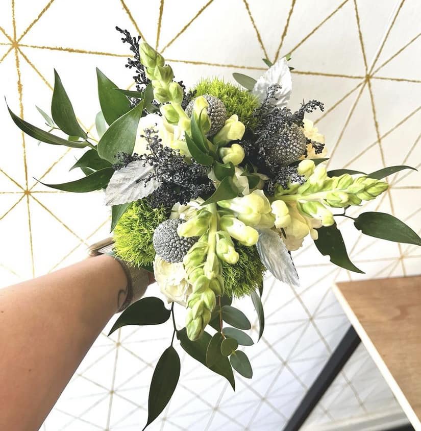 Handheld bouquet with pale yellow flowers, green accents, and silver foliage
