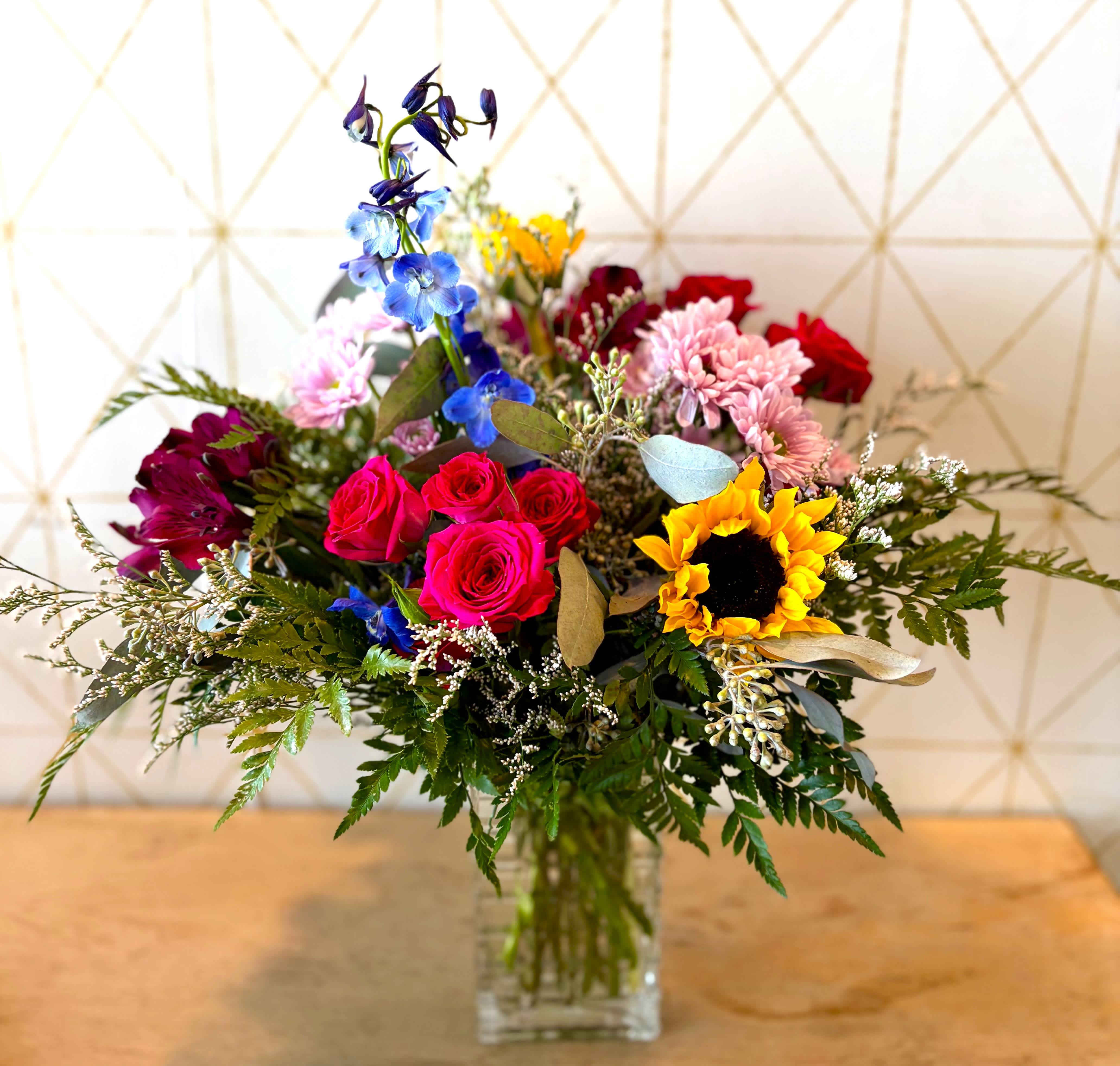 Mixed bouquet with roses, sunflowers, and blue flowers in a glass vase