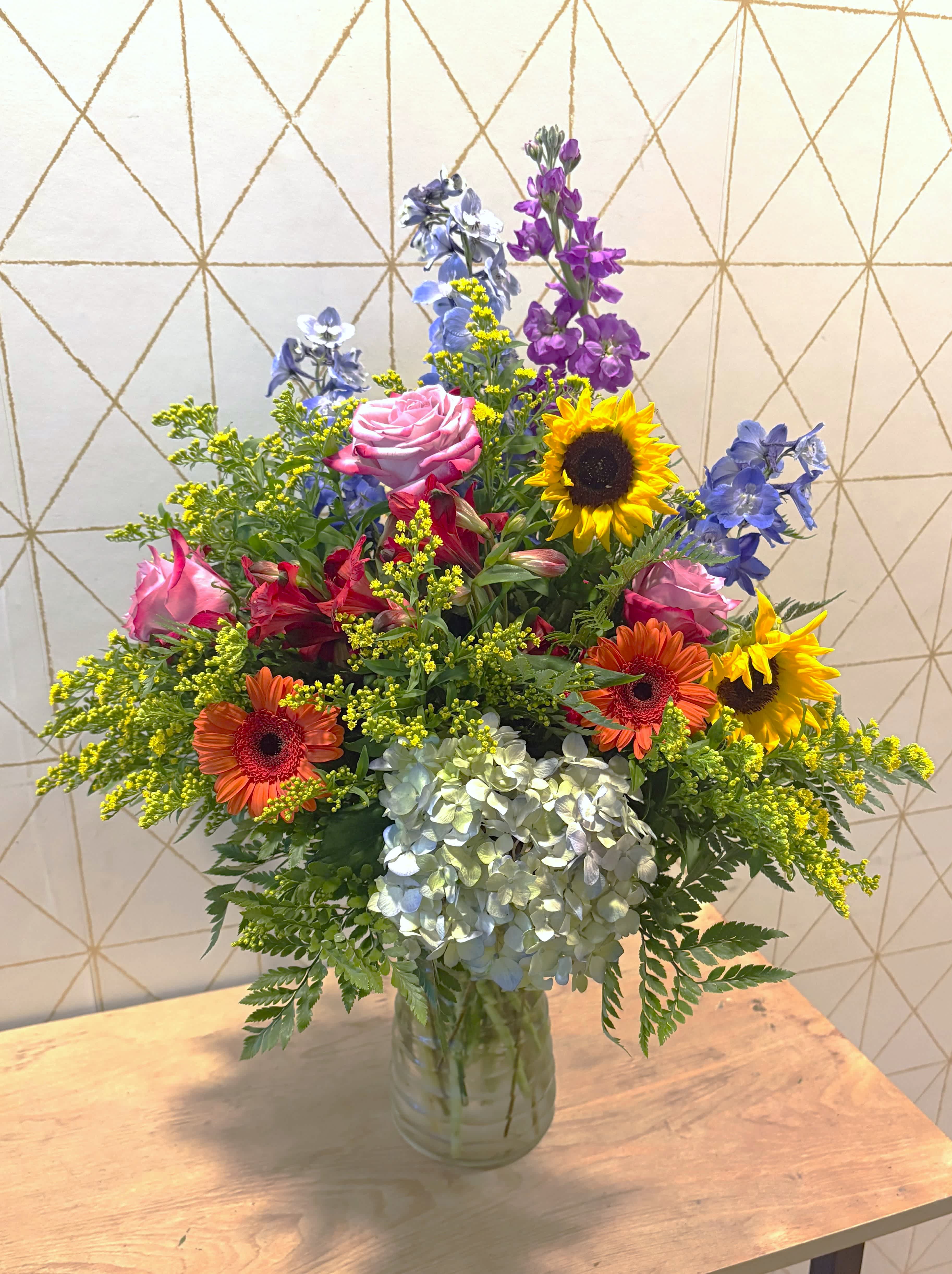 Mixed bouquet in a glass vase with roses, sunflowers, hydrangea, and blue-purple blooms