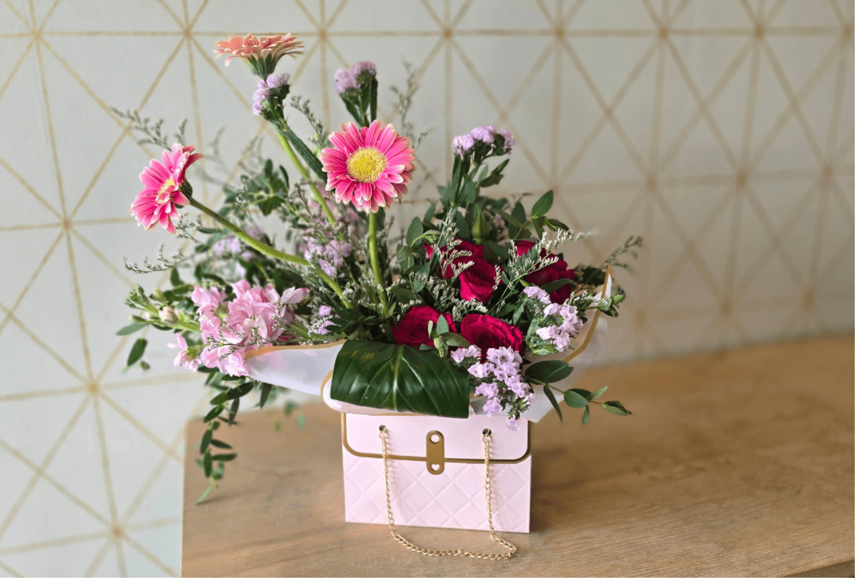 The Kate - A little sweet, stylish and effortlessly fun. The Kate pairs vibrant pink roses and gerbera daisies with soft lavender statice and delicate blooms, all tucked into lush greenery. Finished in a chic handbag-inspired container, this is the perfect gift for someone who deserves a little extra love.
