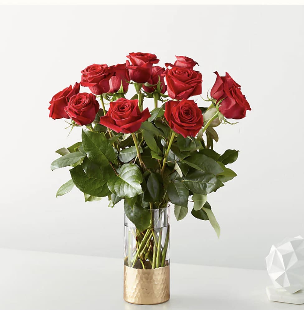Tall arrangement of red roses in a clear glass vase with a gold base
