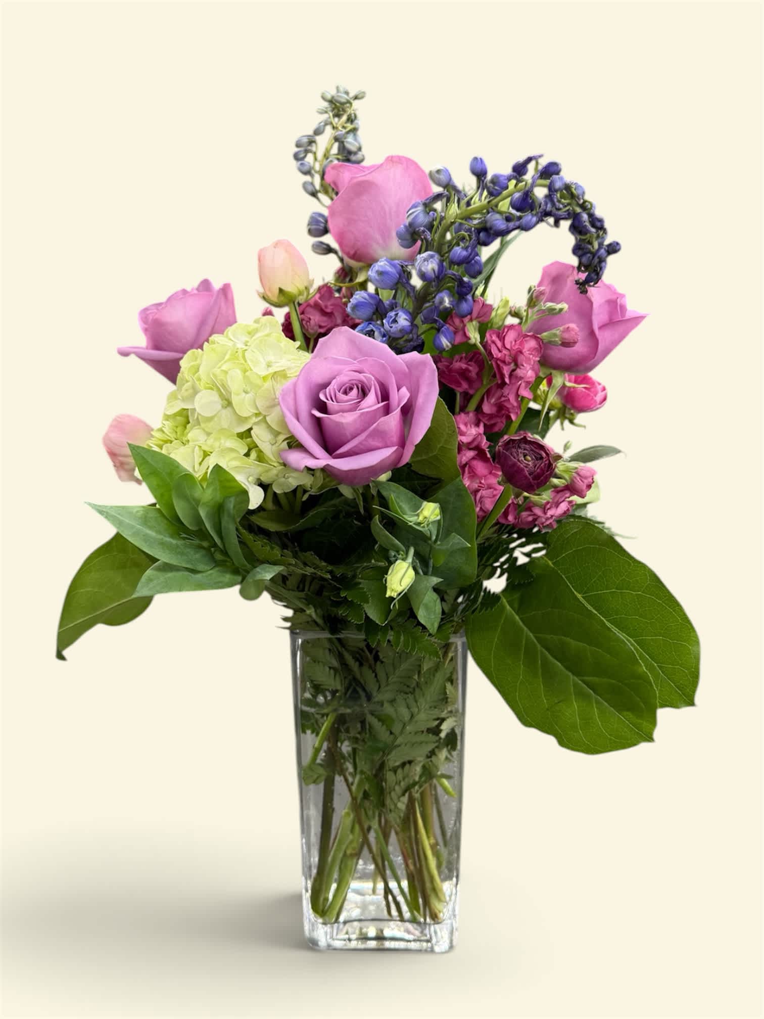 Lavender roses and mixed purple flowers in a clear glass vase
