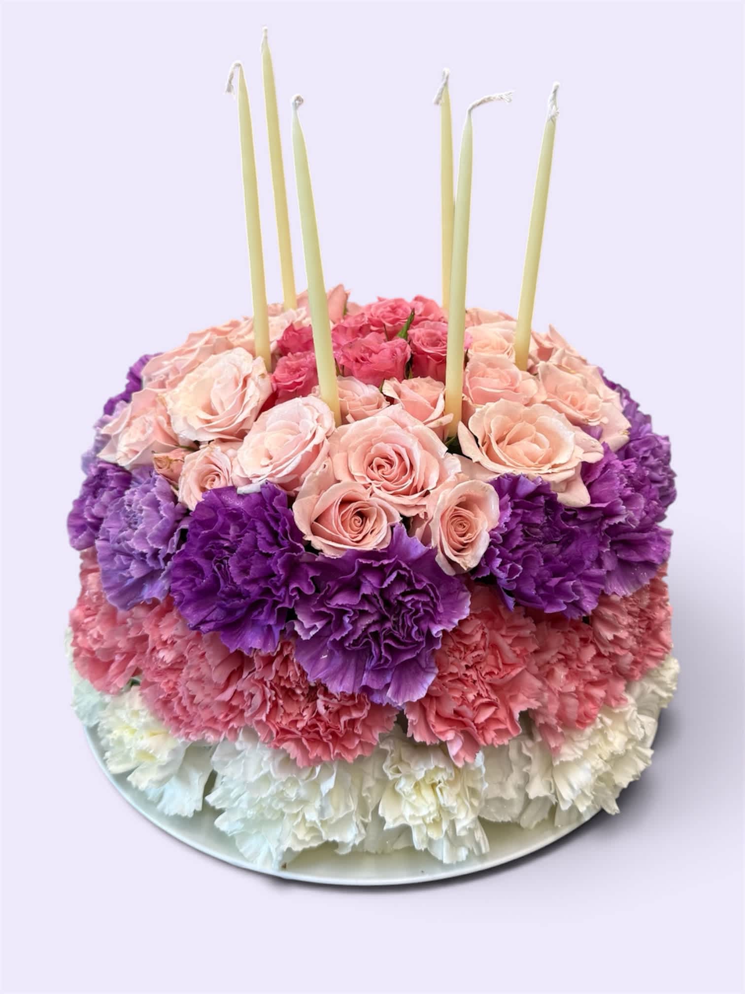 Round floral cake with pink roses, purple carnations, and white candles