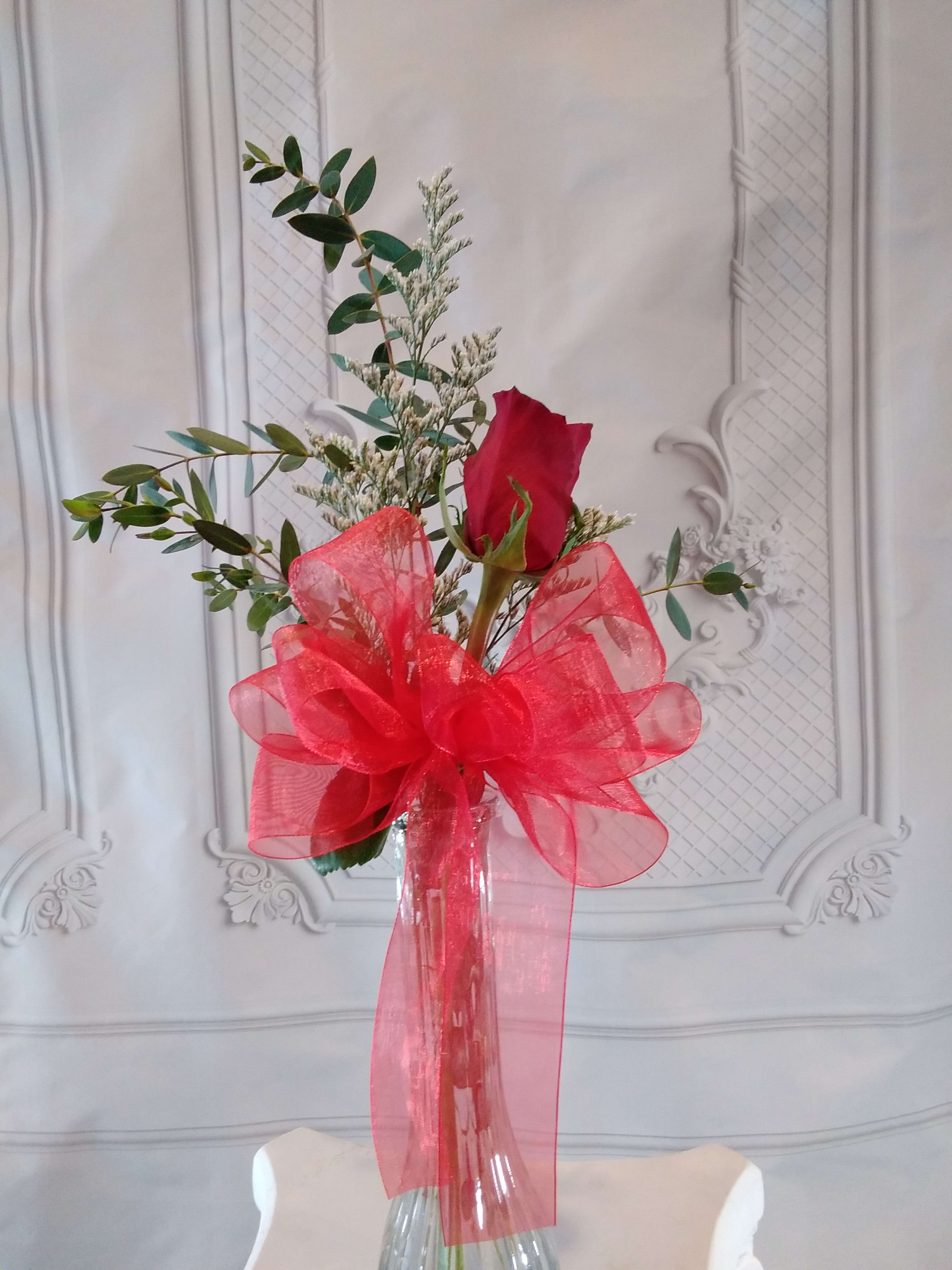Single red rose in a clear vase with a large red bow