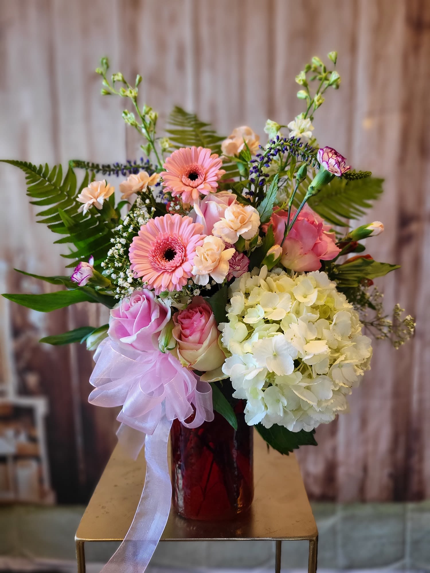 Pink and cream bouquet in a red vase with a lavender ribbon