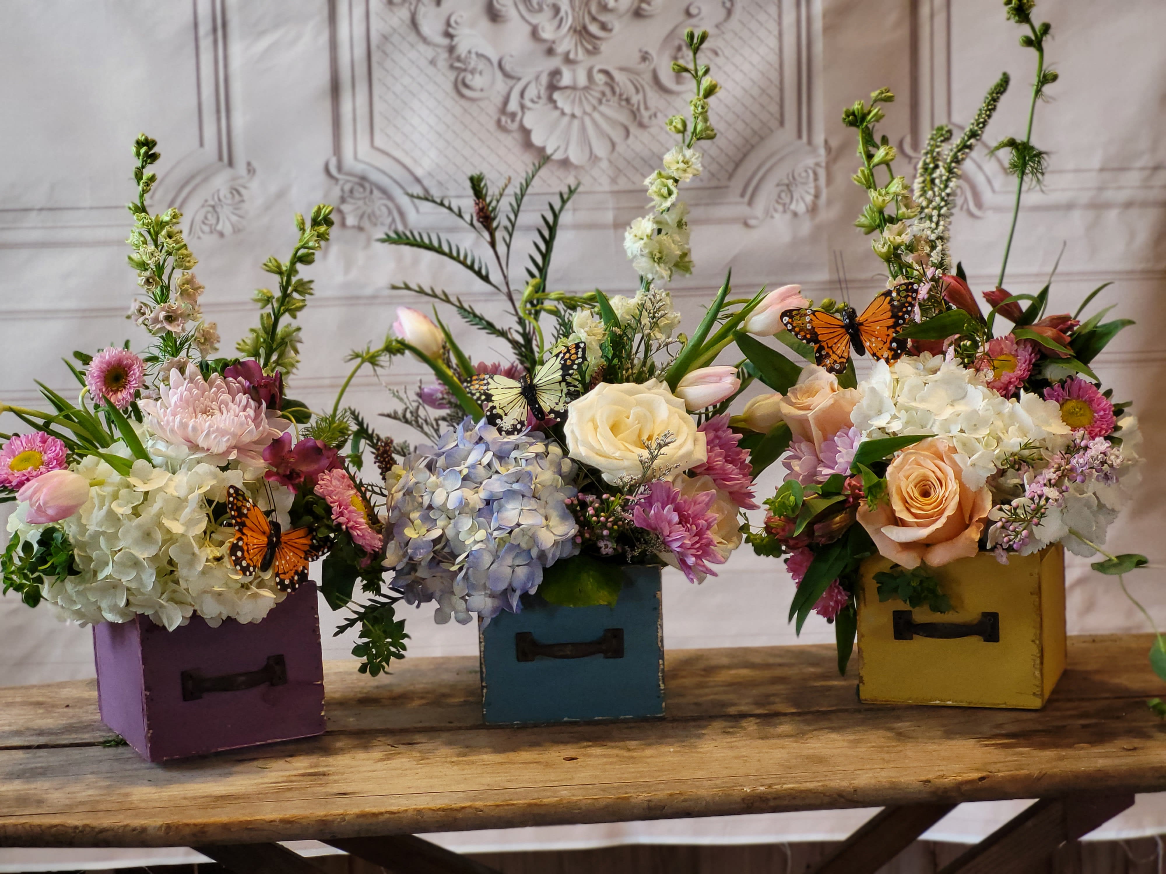 Three floral arrangements in colorful wooden boxes with butterfly accents