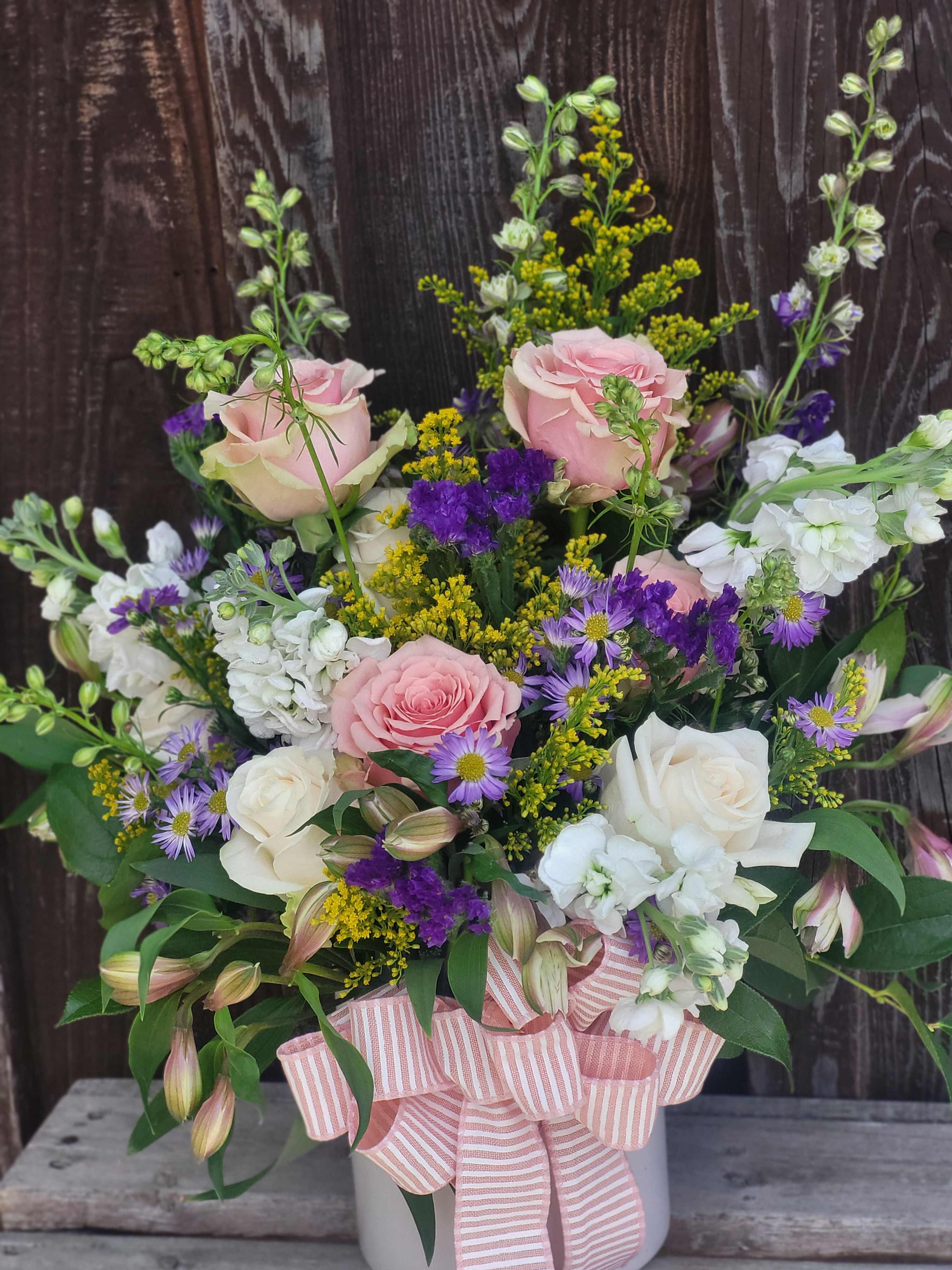 Pink and white roses with purple filler flowers in a white hatbox