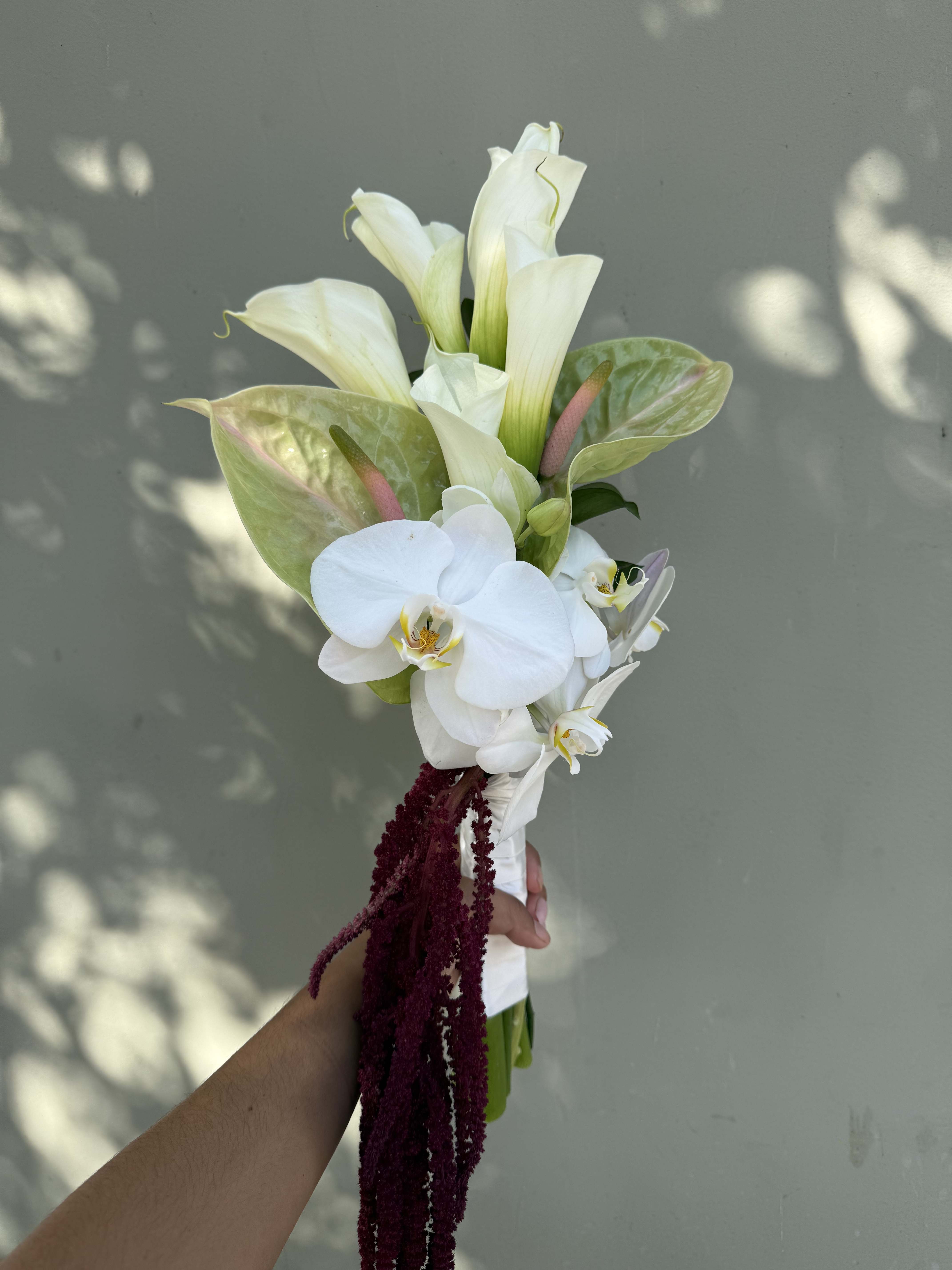 White calla lilies and orchids in a hand-tied bouquet with burgundy trailing accents