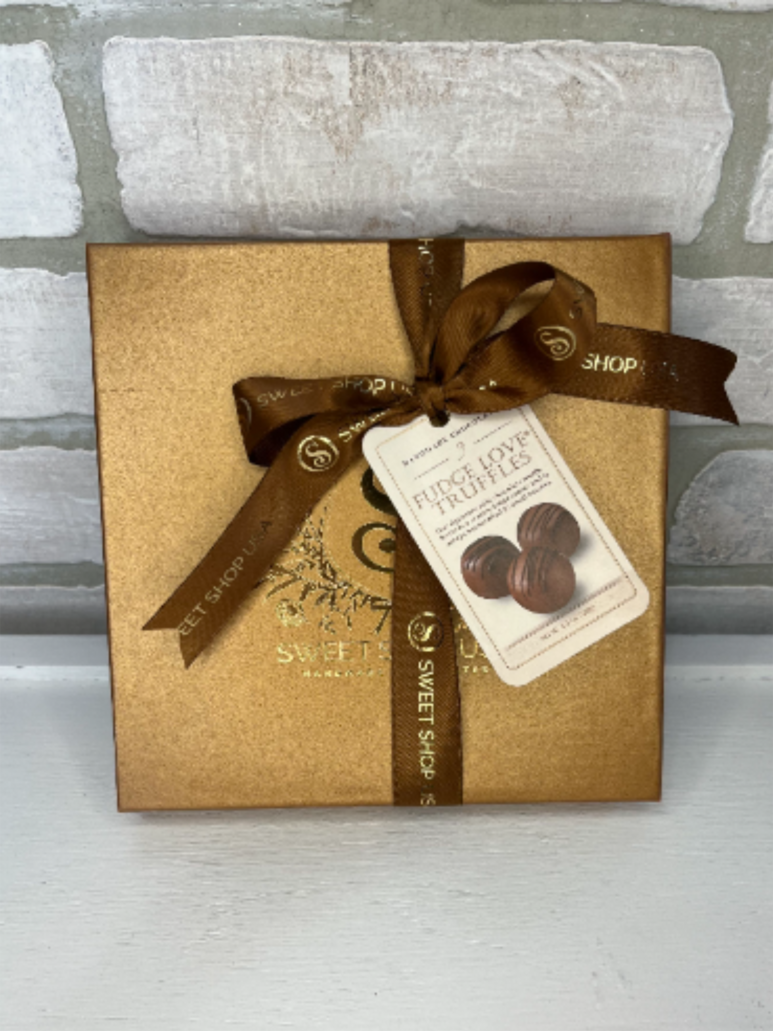 Gold chocolate gift box tied with brown ribbon and a truffle tag on a light background