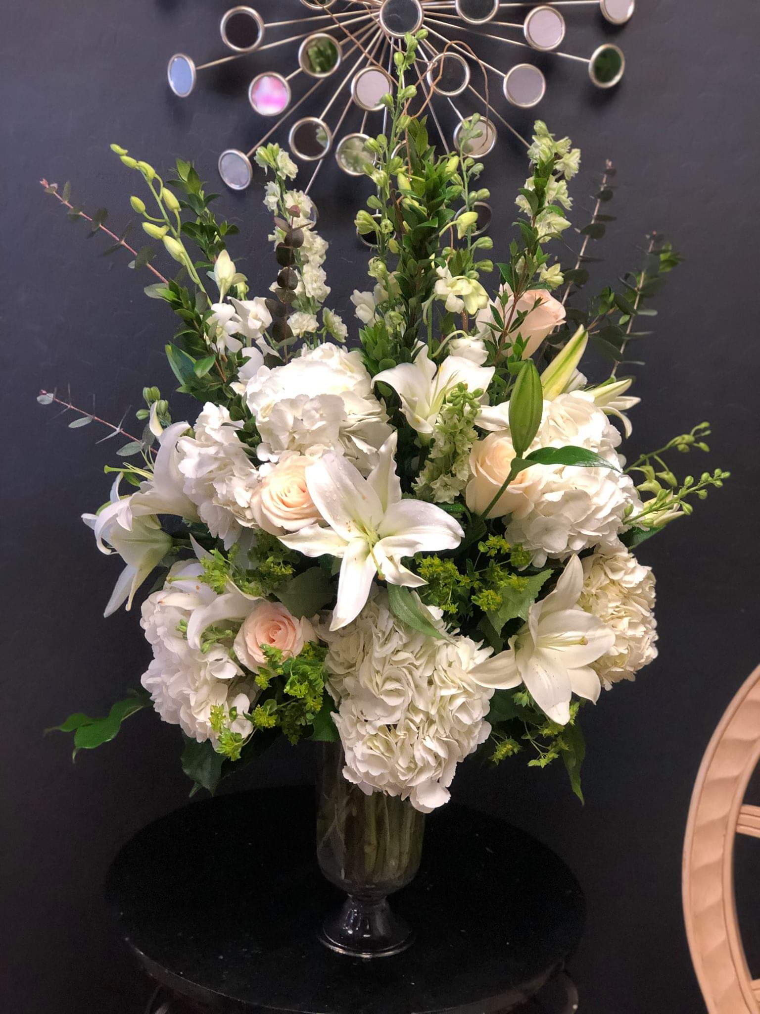 White floral arrangement in a glass vase with lilies, roses, and hydrangeas