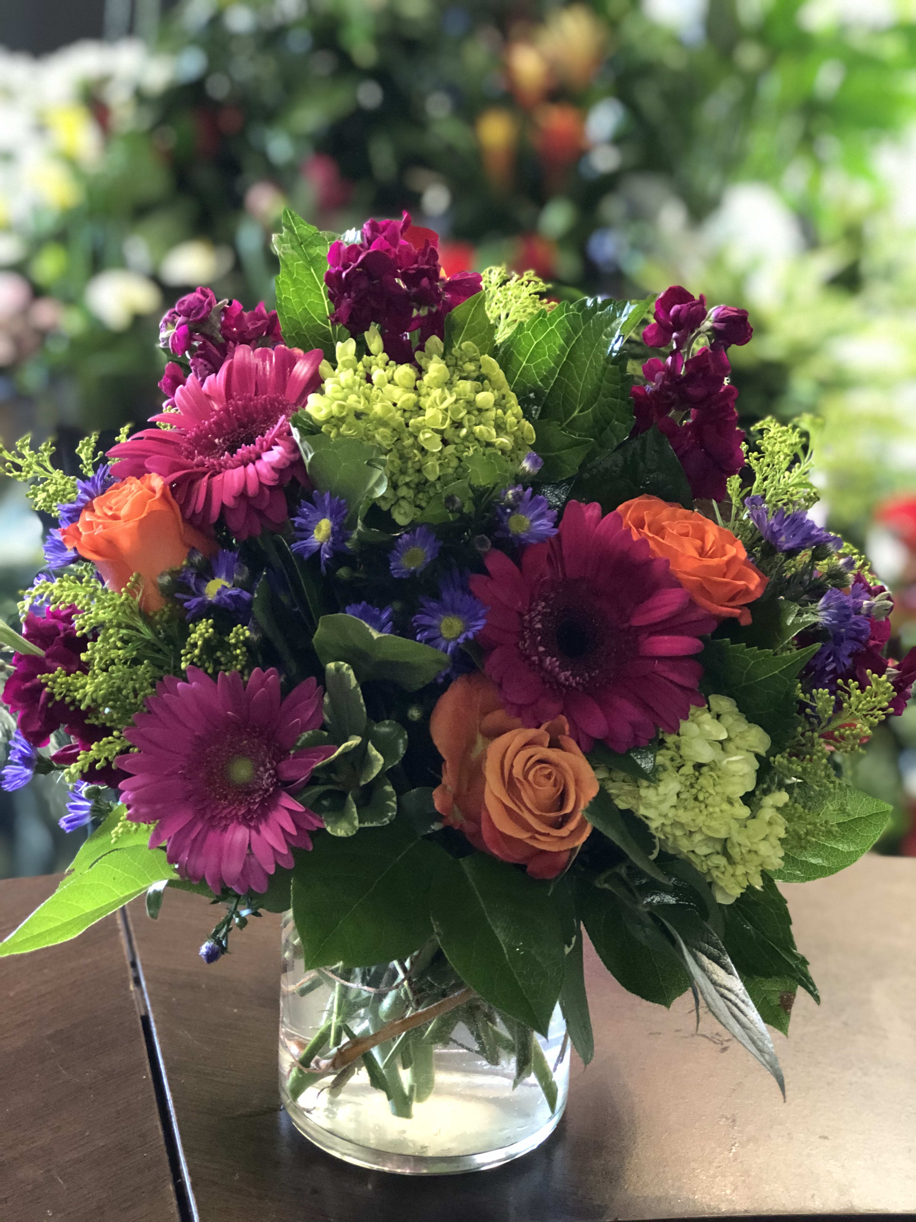 Mixed bouquet of magenta, orange, and purple flowers in a glass vase