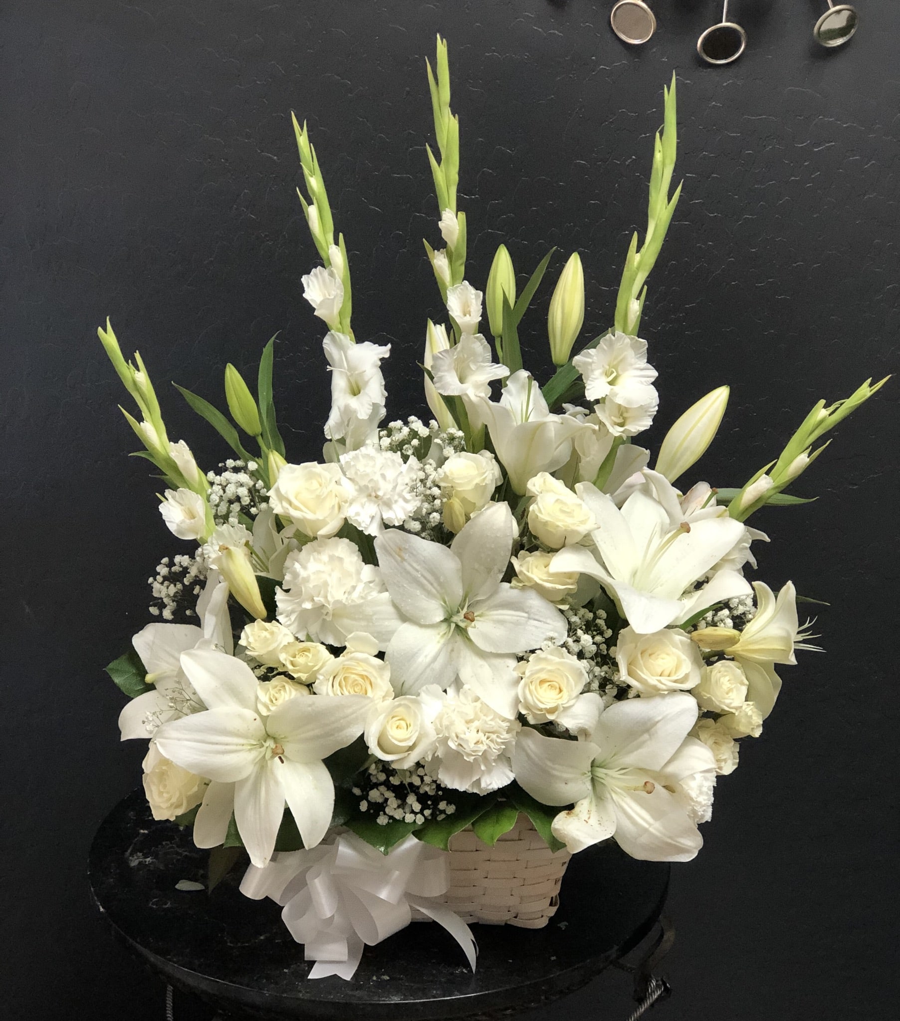 The FTD Peaceful Passage Arrangement - Let this exquisite bouquet deliver your sincere condolences at this time of loss and sadness. An always-appropriate mixed bouquet of white roses carnations gladioli football chrysanthemums LA hybrid lilies and million star gypsophelia plus an assortment of lush greens comes hand-arranged in a charming white wood chip basket by a local FTD artisan florist. This versatile arrangement is perfect for display on a table floor or pedestal at a funeral home on an altar floor or sanctuary steps for a funeral and graveside at a burial ceremony.