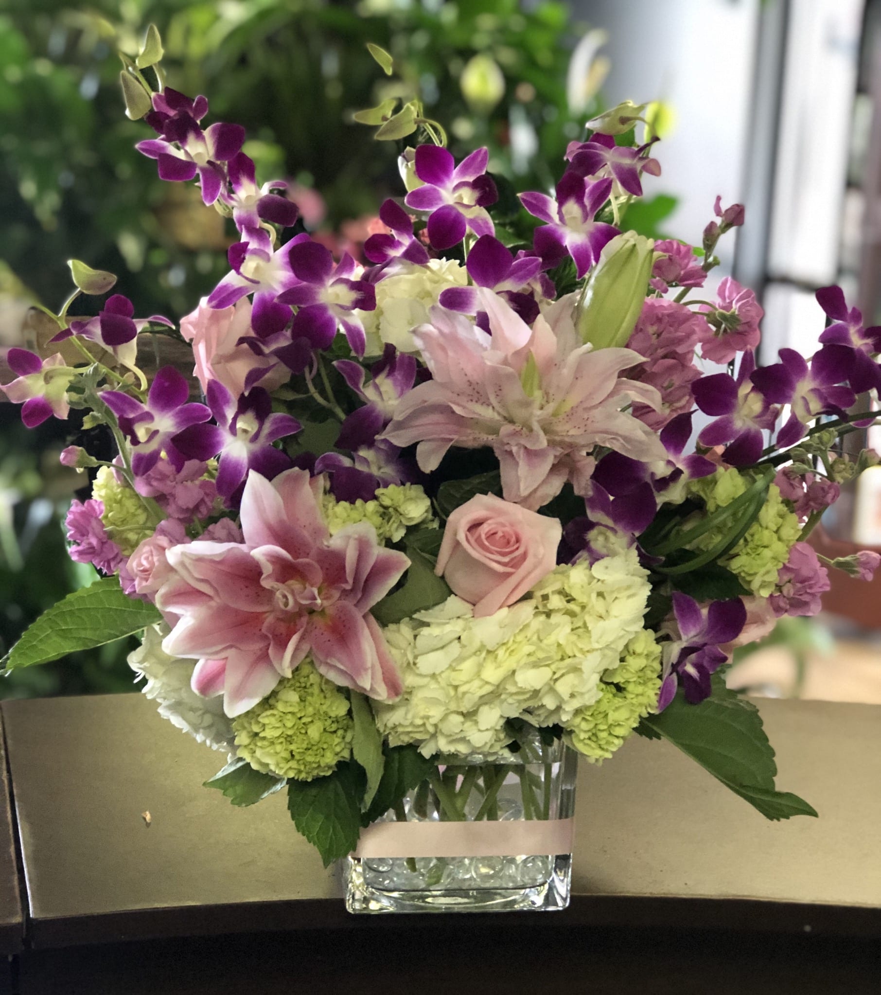 Pink lilies, roses, hydrangeas, and purple orchids in a clear glass vase