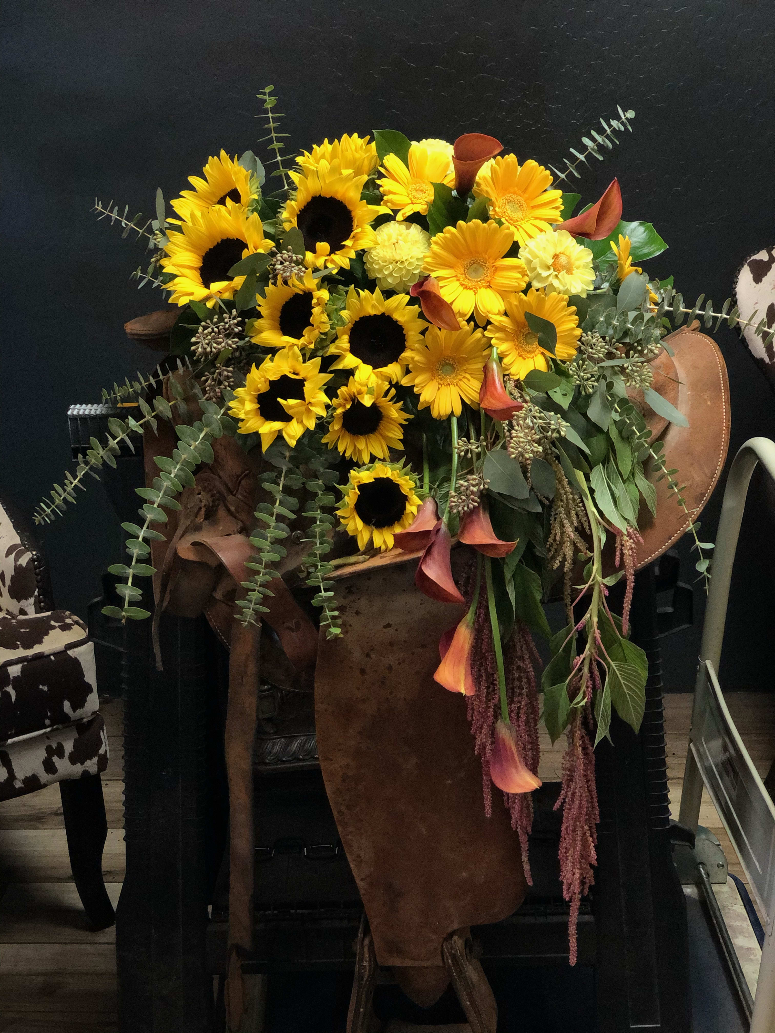 Large bouquet of yellow sunflowers and orange calla lilies in a rustic container