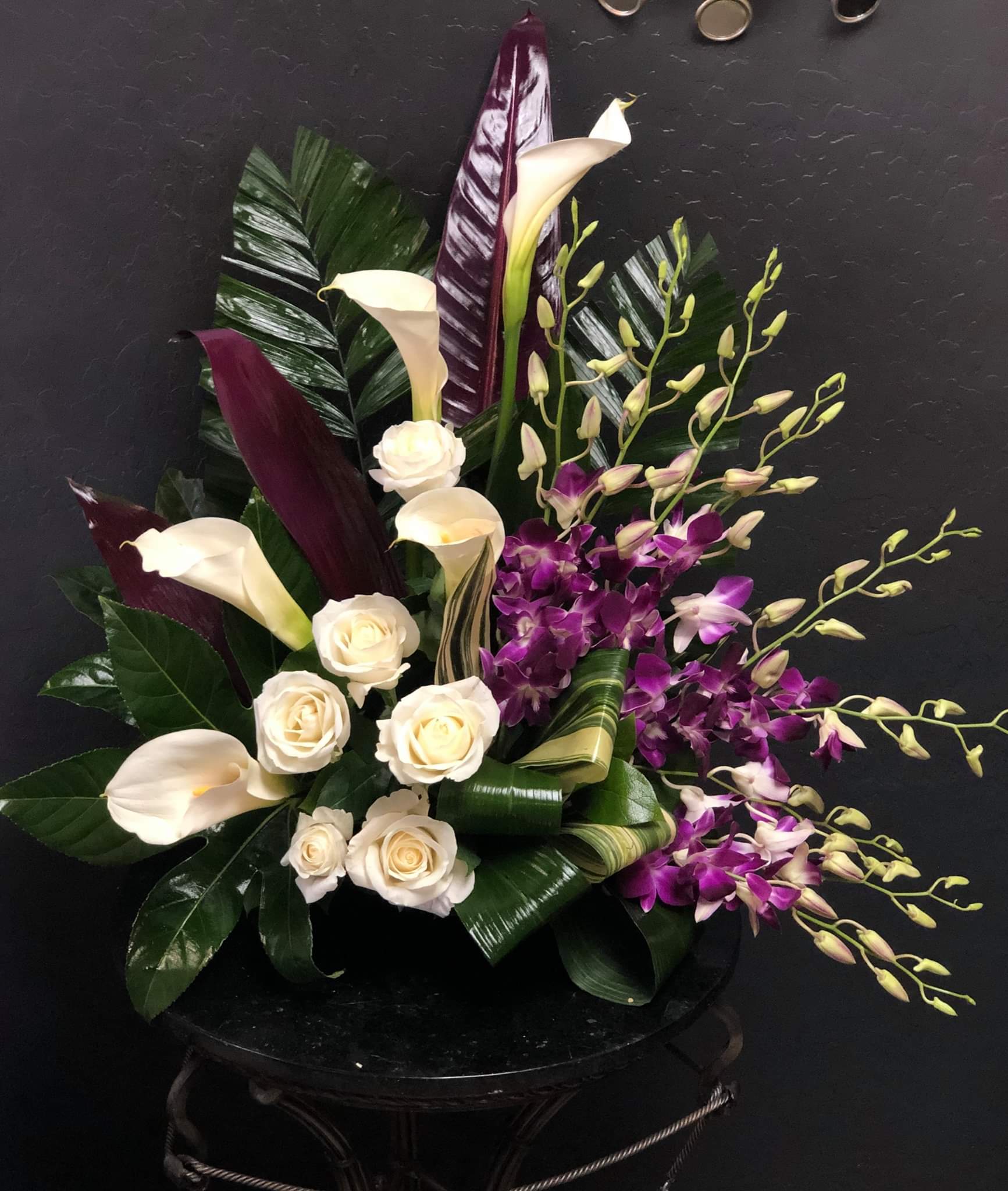 Arrangement of white calla lilies, cream roses, and purple orchids