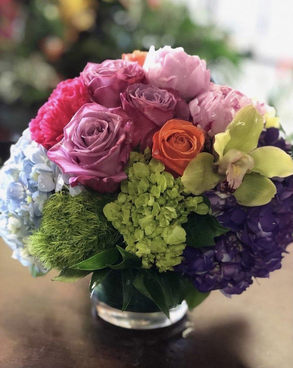 Colorful bouquet of roses, hydrangeas, and orchids in a glass vase