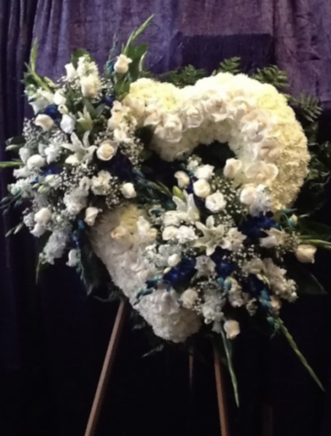 Large white floral funeral wreath on an easel with blue accents