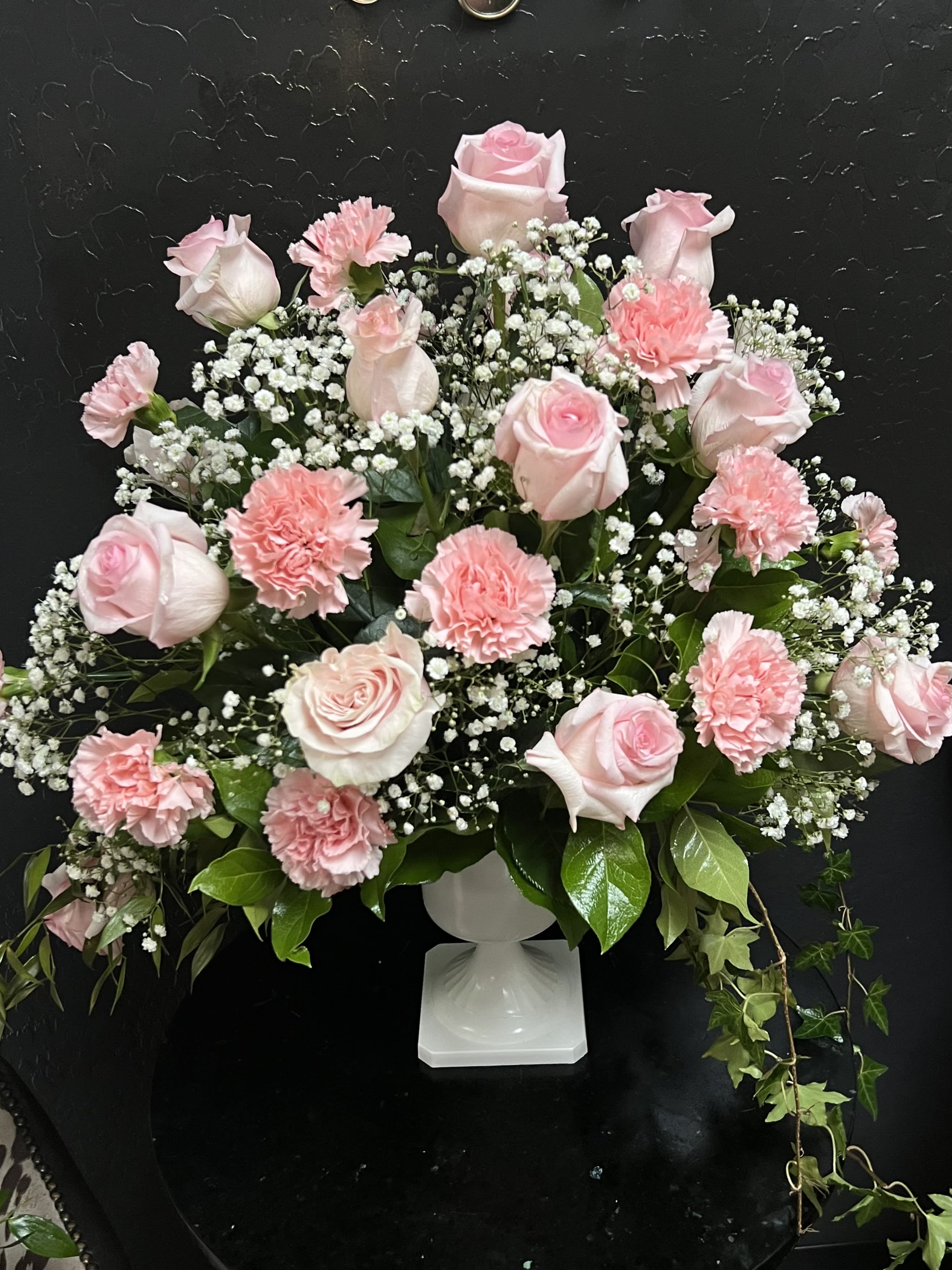Pink roses and carnations arranged in a white pedestal vase