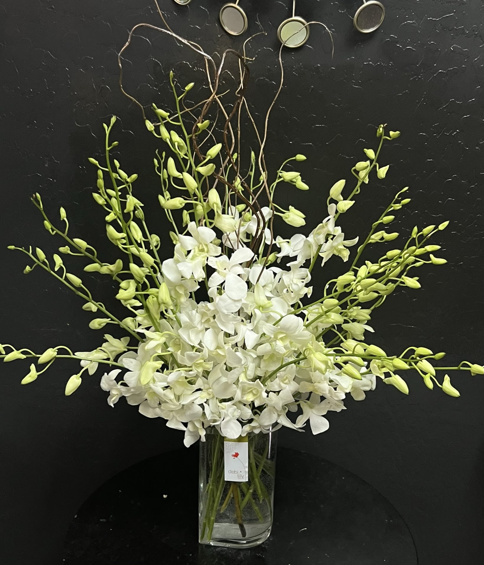 White orchid arrangement in a clear glass vase with arching green buds