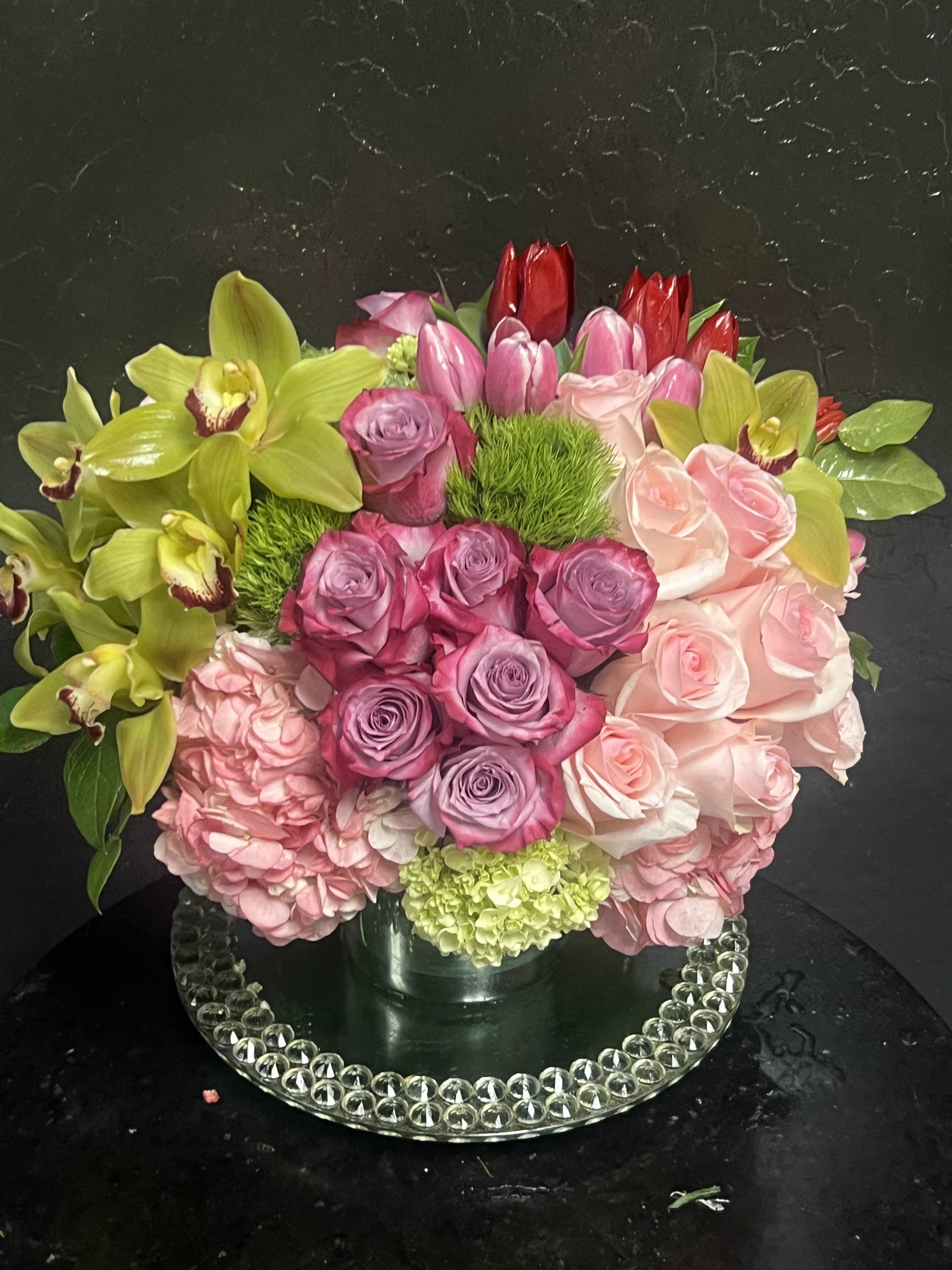 Mixed bouquet of pink roses, hydrangeas, tulips, and green orchids in a vase