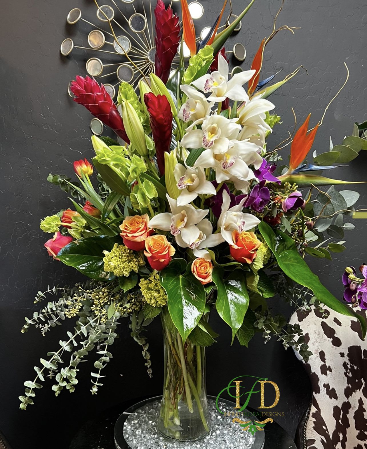 Tall mixed bouquet with white orchids, orange roses, and red tropical blooms in a glass vase