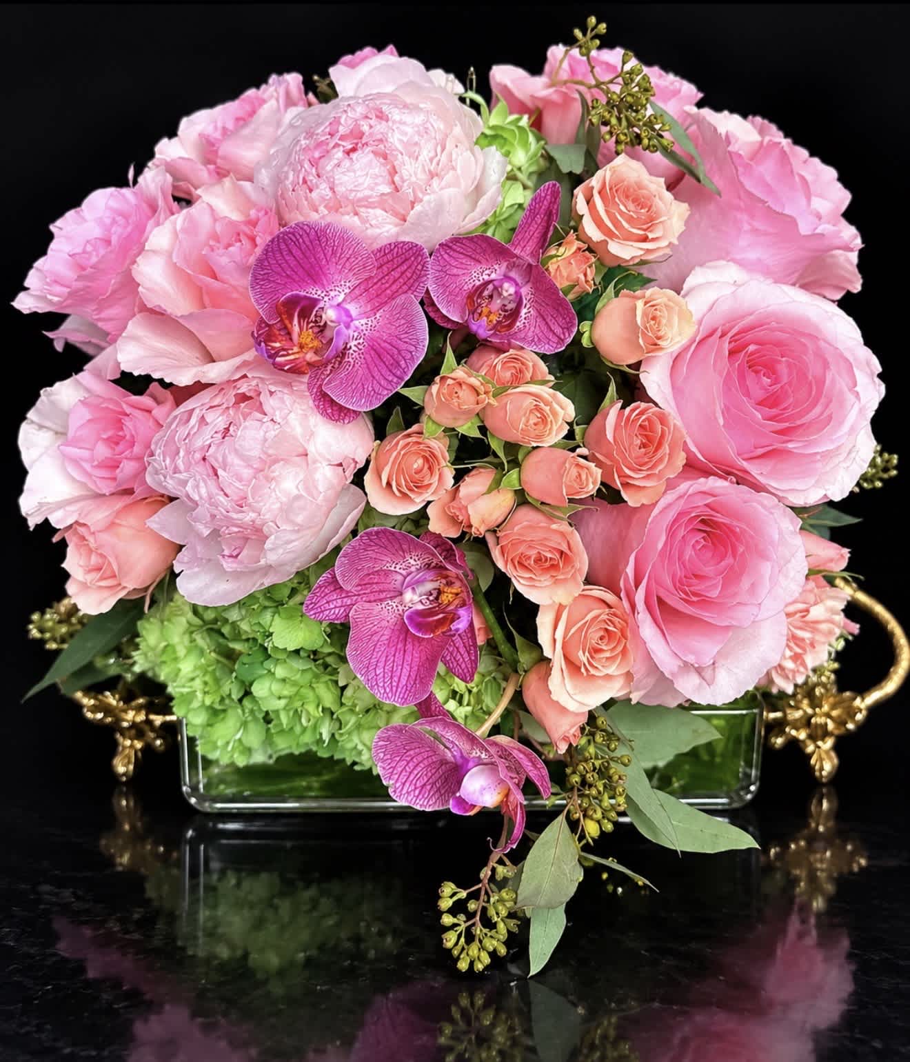 Pink roses and orchids arranged in a glass vase with green hydrangea
