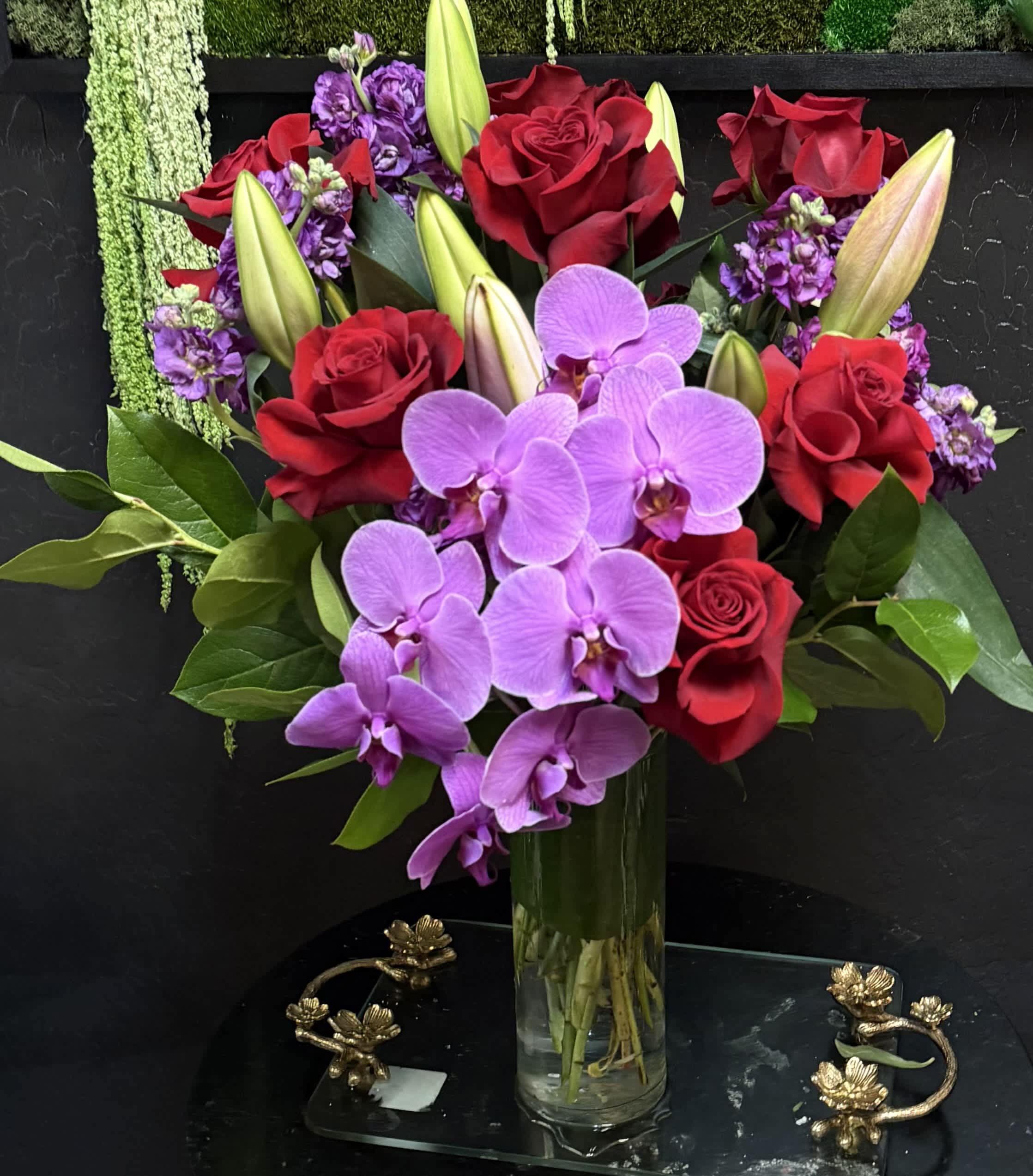 Bouquet of red roses, purple orchids, and lilies in a glass vase