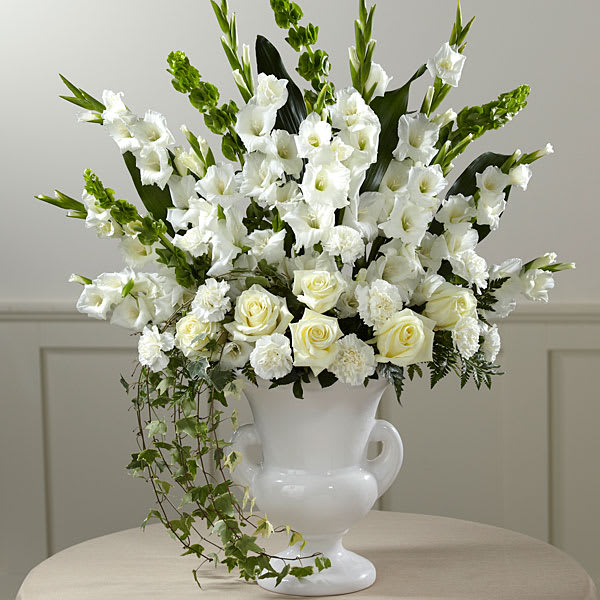 The FTD Fond Reflections Arrangement - An expression of sympathy that’s tasteful dignified and with a beautiful sensibility that conveys your feelings with warmth and sincerity. This generously-scaled arrangement makes a superb choice with hand-selected white gladioli carnations roses and Bells of Ireland complemented with lush greenery by an FTD local artisan florist and arranged in a classic white ceramic urn. Its comforting presence and impressive scale makes a fitting tribute for a wake the funeral service or to add a note of serene consolation to a graveside service.