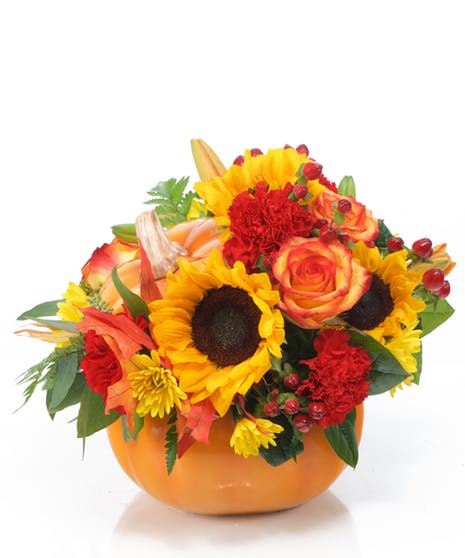 Autumn bouquet of sunflowers, roses, and carnations in an orange bowl vase
