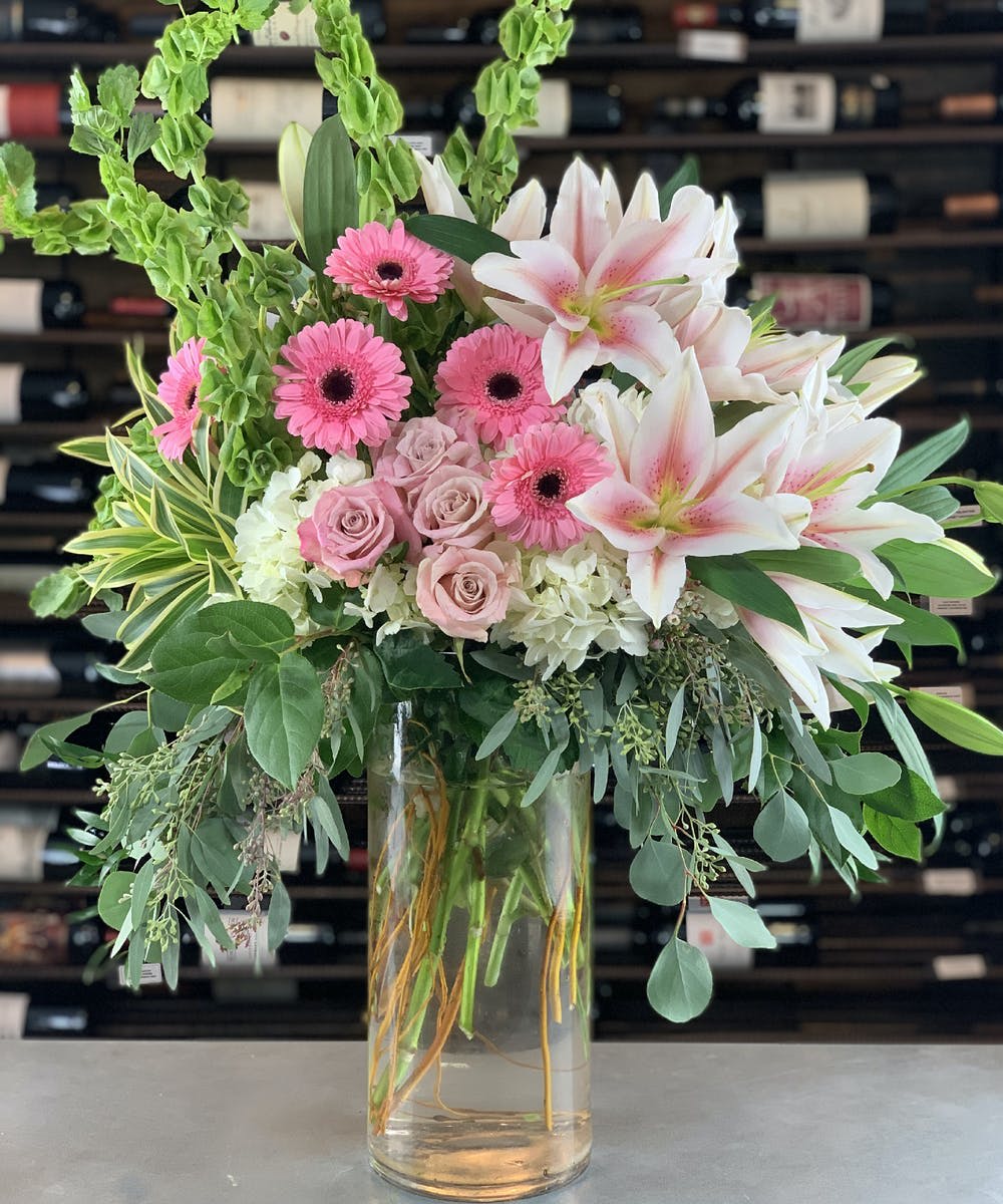 Pink gerberas and lilies in a clear glass vase with greenery