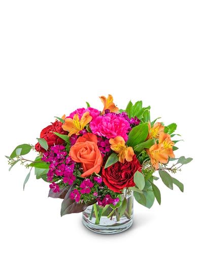 Mango Sunrise - Mango Sunrise may look good enough to eat but it's even more beautiful to display. This vibrant contains orange roses, carnations, alstroemeria, and accented with a variety of foliage in a clear vase. 