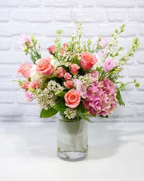 Pink and peach roses with hydrangea in a clear glass vase