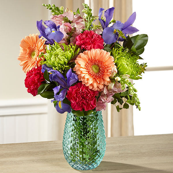 The FTD Joyful Moments Bouquet by Better Homes and Gardens - This bouquet includes: peach gerbera daisies, light blue iris, pink snapdragons, hot pink carnations, green and yellow buplerum, and fresh greens. Presented in a vintage inspired clear glass vase.