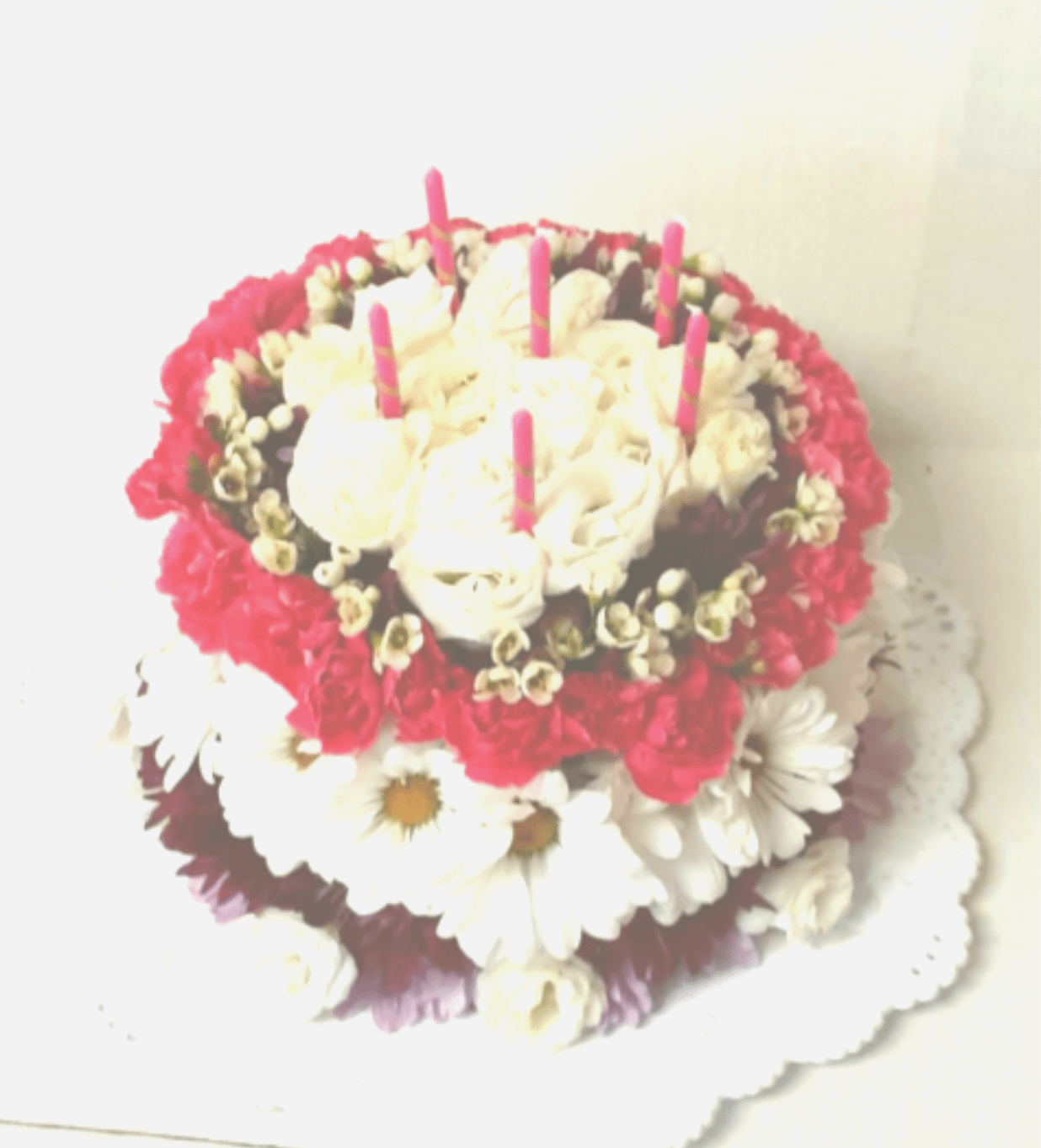 Round floral cake with white roses, daisies, and pink candles
