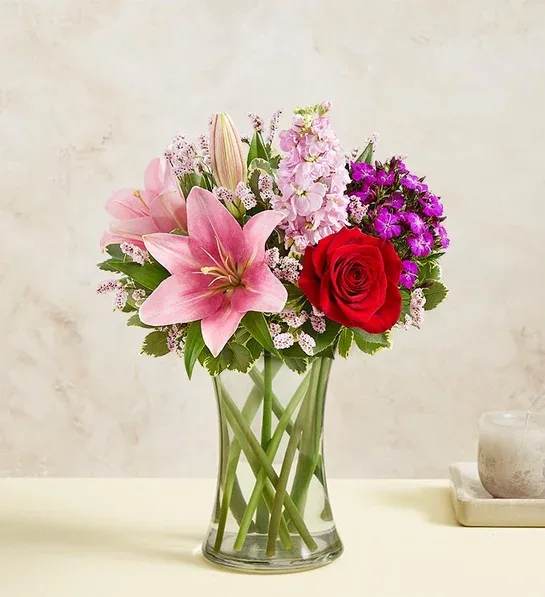 Pink lilies and a red rose in a clear glass vase