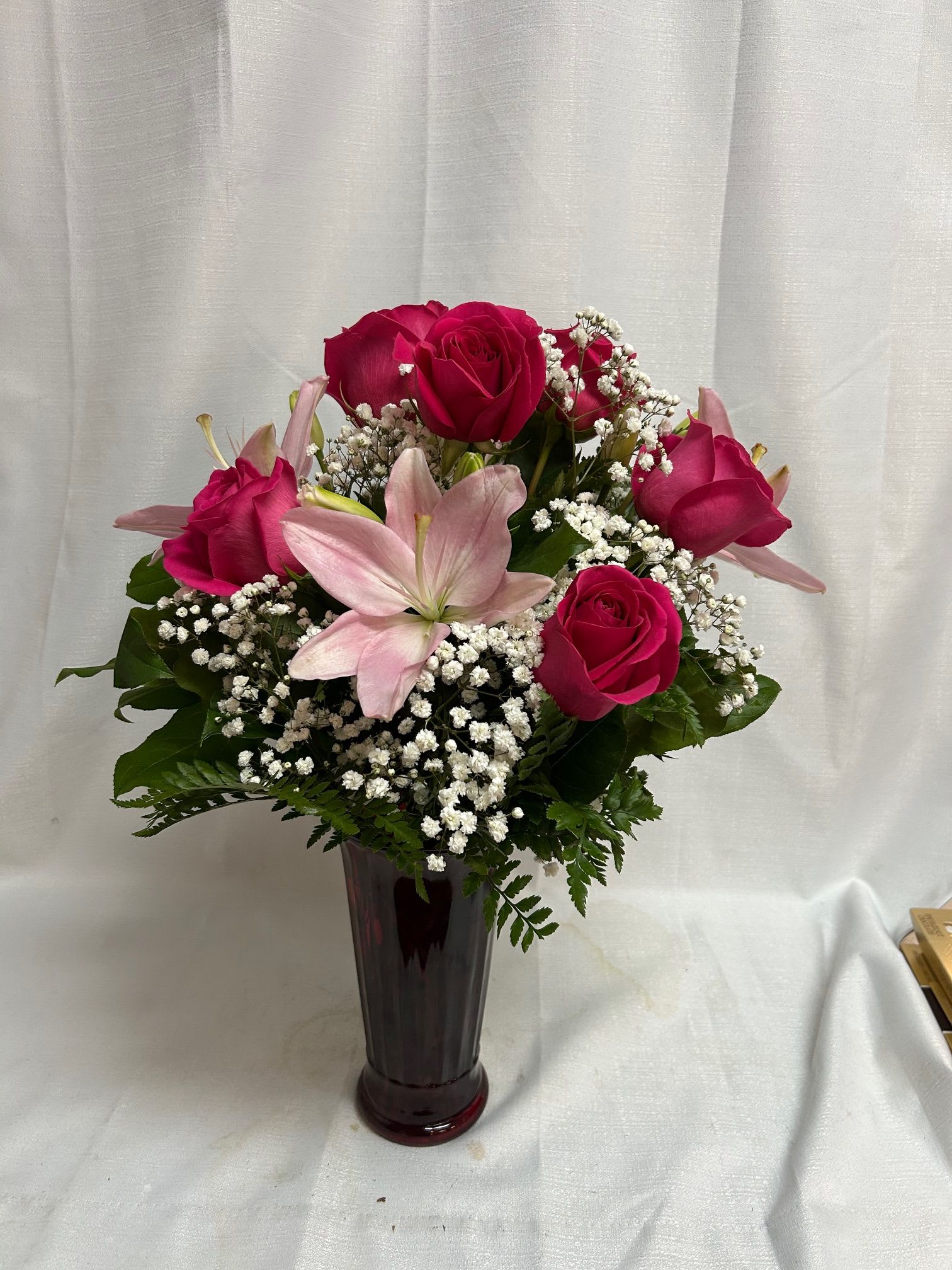 Pink roses and a pale lily arranged in a tall vase