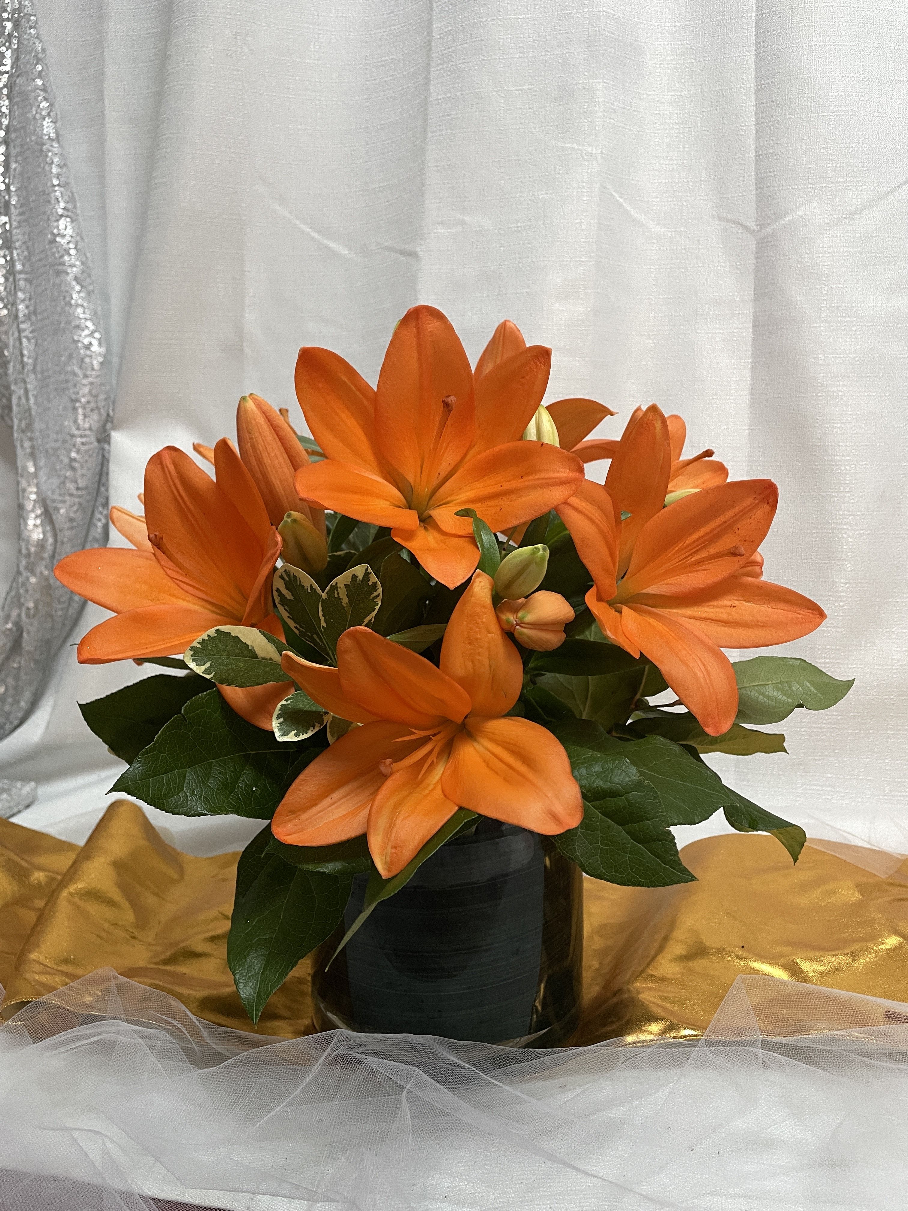 Orange lilies arranged in a black vase with dark green foliage