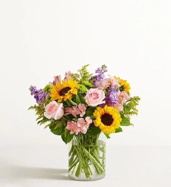 Garden Of Grandeur - Designed to be as unforgettable as the person who receives it. Our luxurious arrangement of colorful, fresh-from-the-garden blooms is artistically arranged inside a chic cylinder vase by our expert florists to create the ultimate wow gift for someone who means the world to you. All-around arrangement with pink roses and Peruvian lilies (alstroemeria), sunflowers, lavender stock, Athos poms; accented with assorted greenery Artistically designed in a glass cylinder vase;  Large arrangement measures approximately 22"H x 17"W, comes in 12" vase Medium arrangement measures approximately 21.5"H x 16.5"W, comes in 8" vase Small arrangement measures approximately 21"H x 16"W, comes in 8" vase