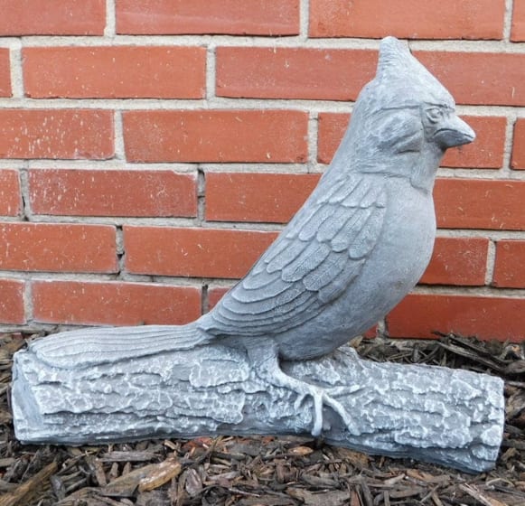 Gray bird statue perched on a faux log against a brick wall