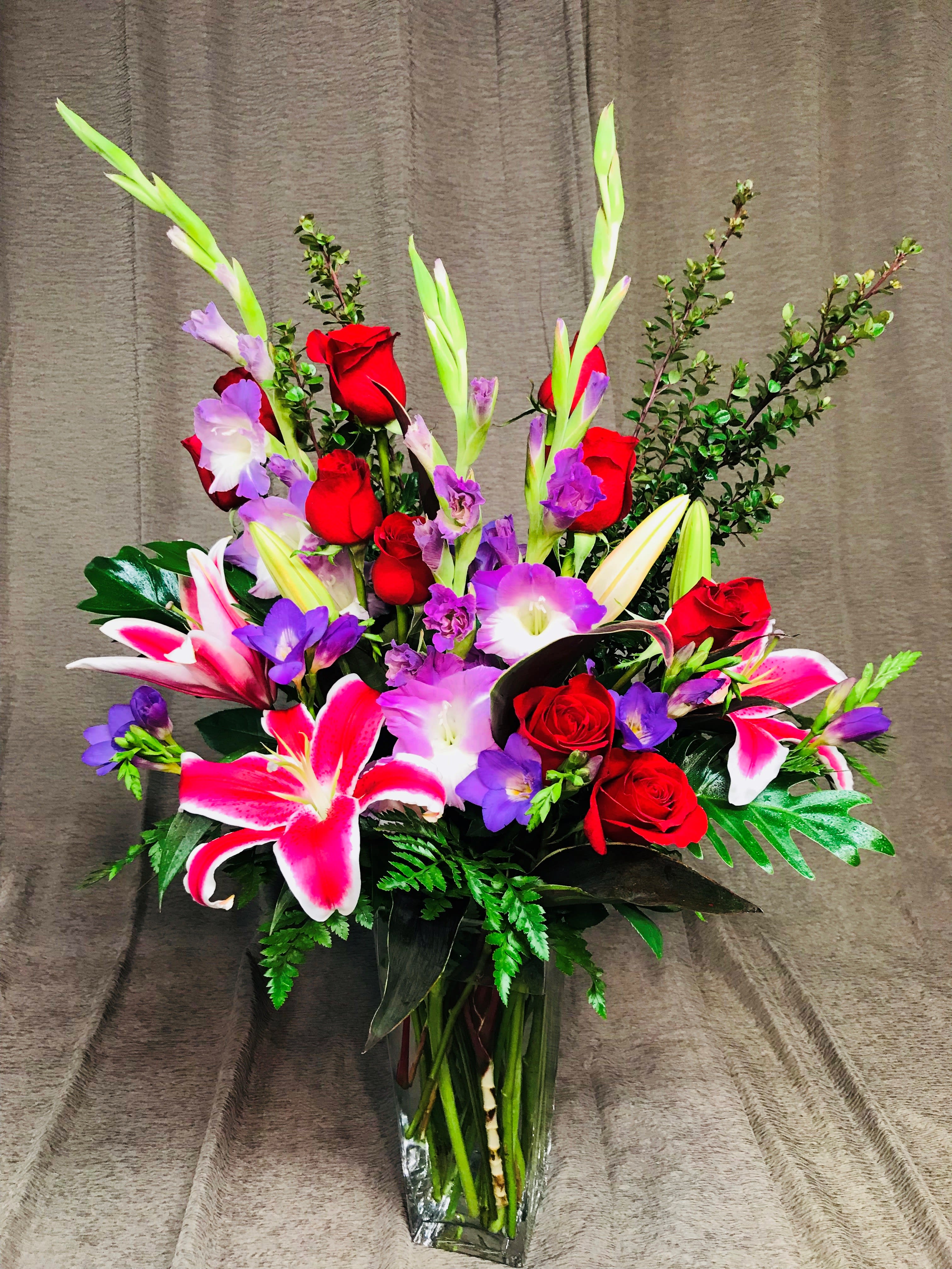 Bouquet of red roses, pink lilies, and purple flowers in a glass vase