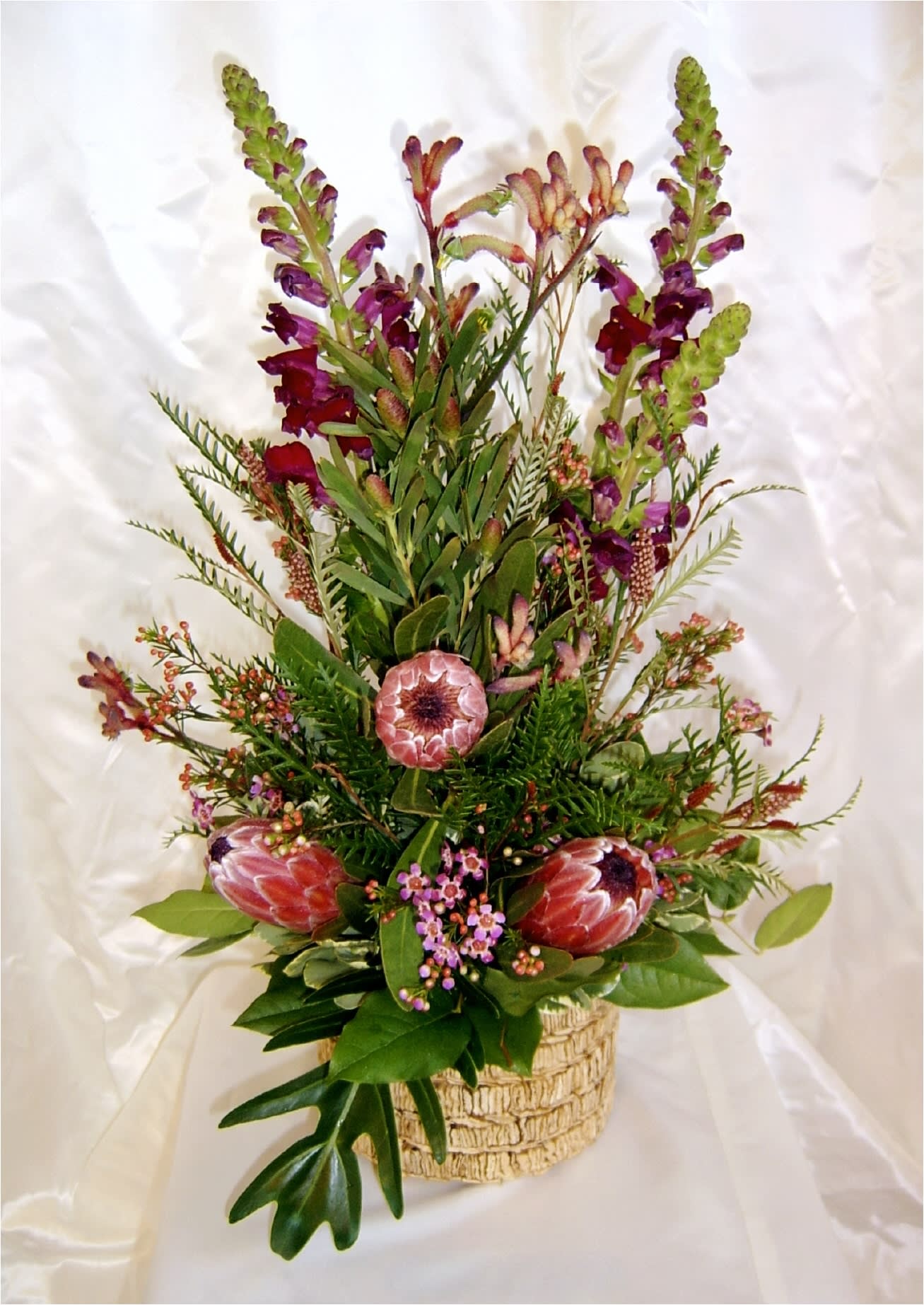 Tall floral arrangement with pink protea and purple snapdragons in a woven basket